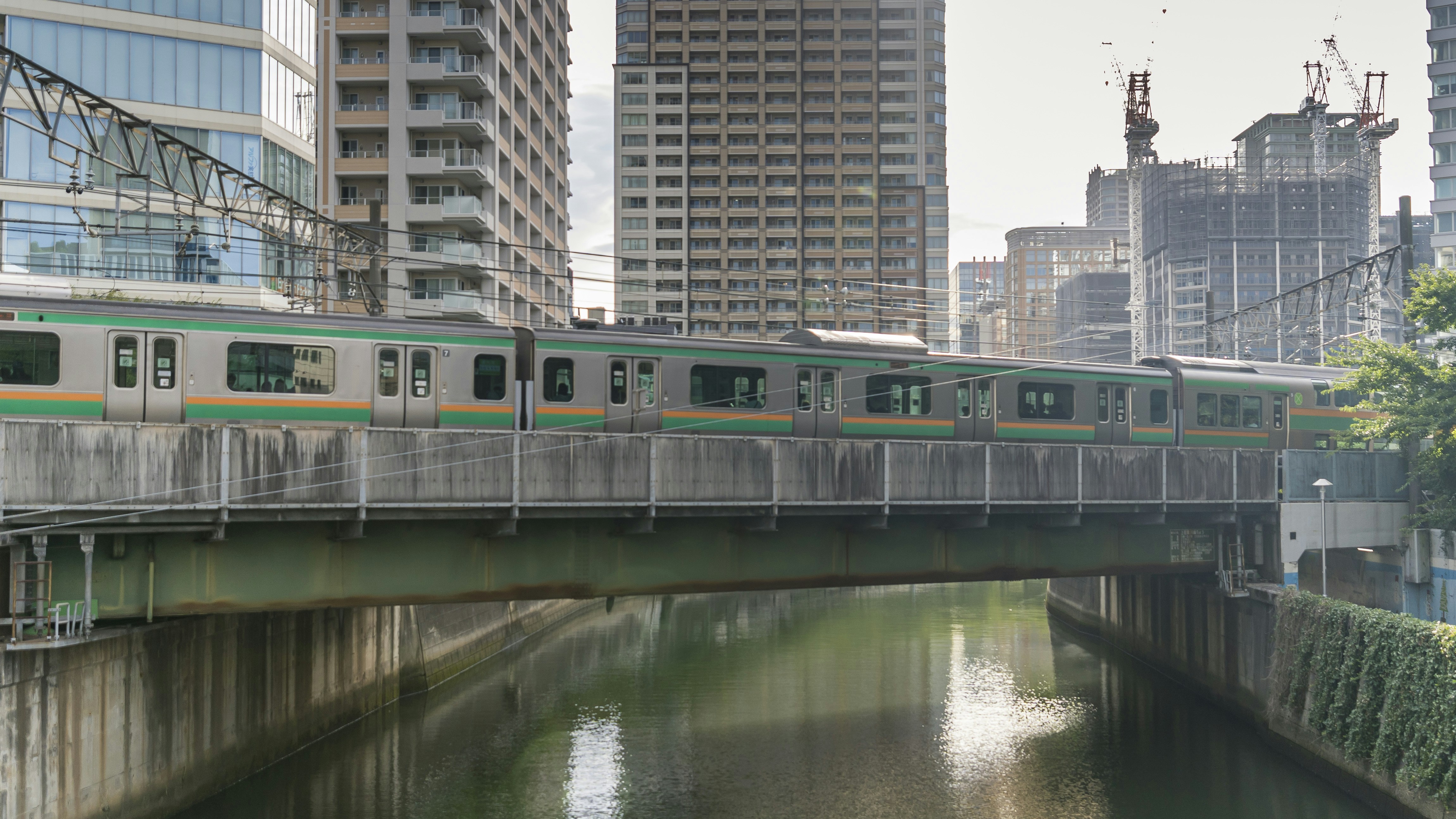 Green train crosses bridge over canal in city.