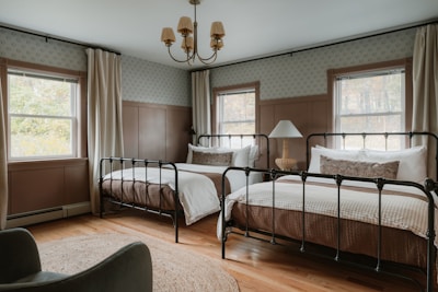 Two beds in a rustic bedroom with windows.