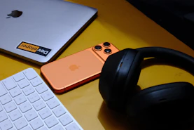 Laptop, phone, keyboard, and headphones on yellow surface