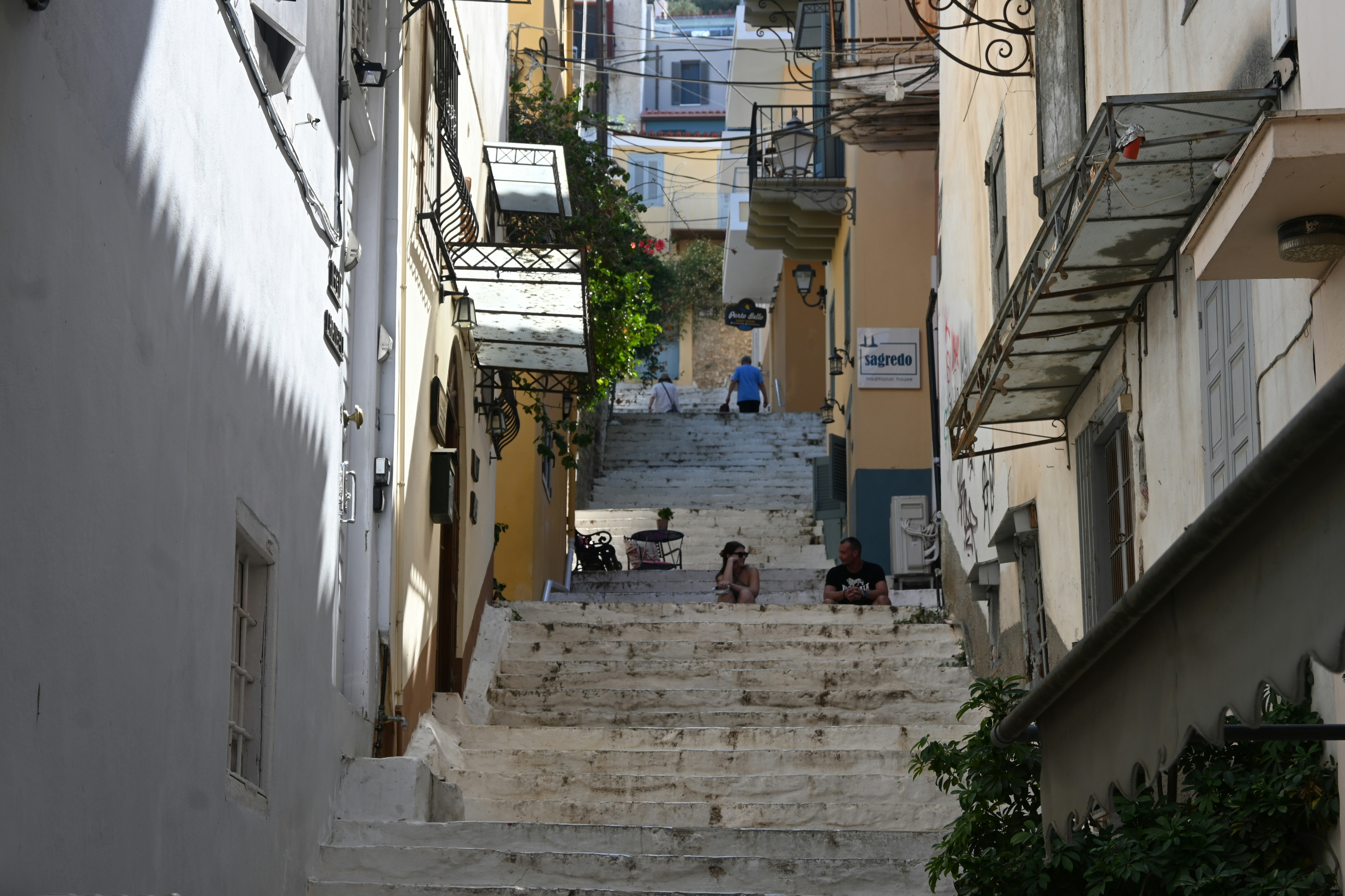 People sit on wide stone steps in a narrow alley.