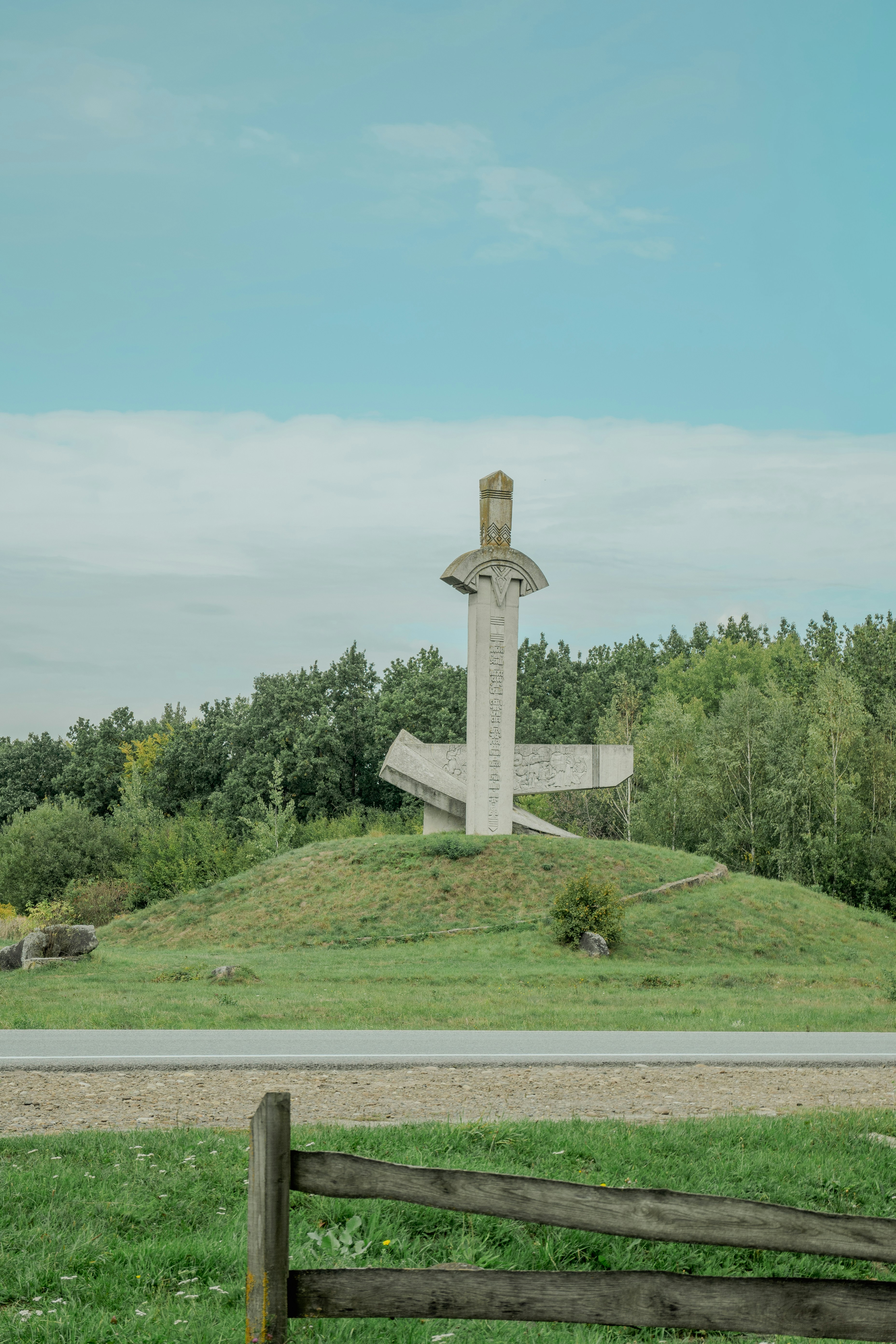 Monumental sword sculpture on grassy hill under sky