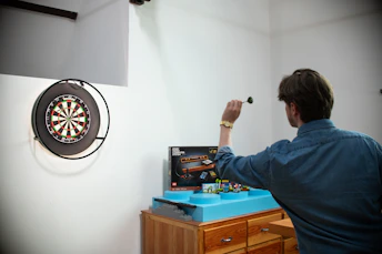 Man throwing dart at dartboard in room.