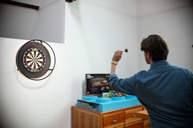 Man throwing dart at dartboard in room.