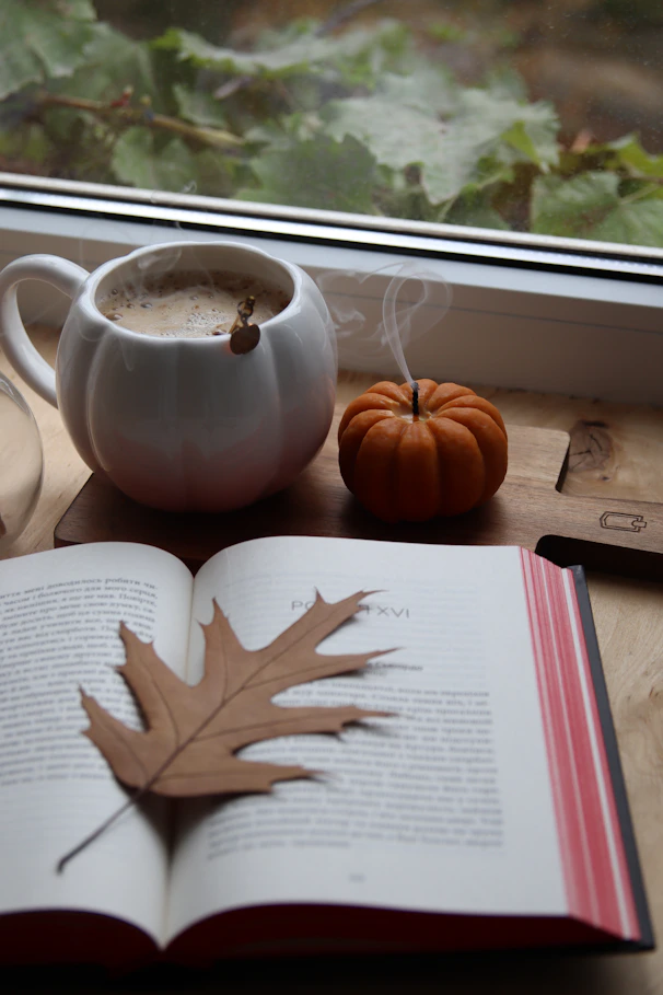 Cozy autumn scene with coffee, book, and pumpkin.