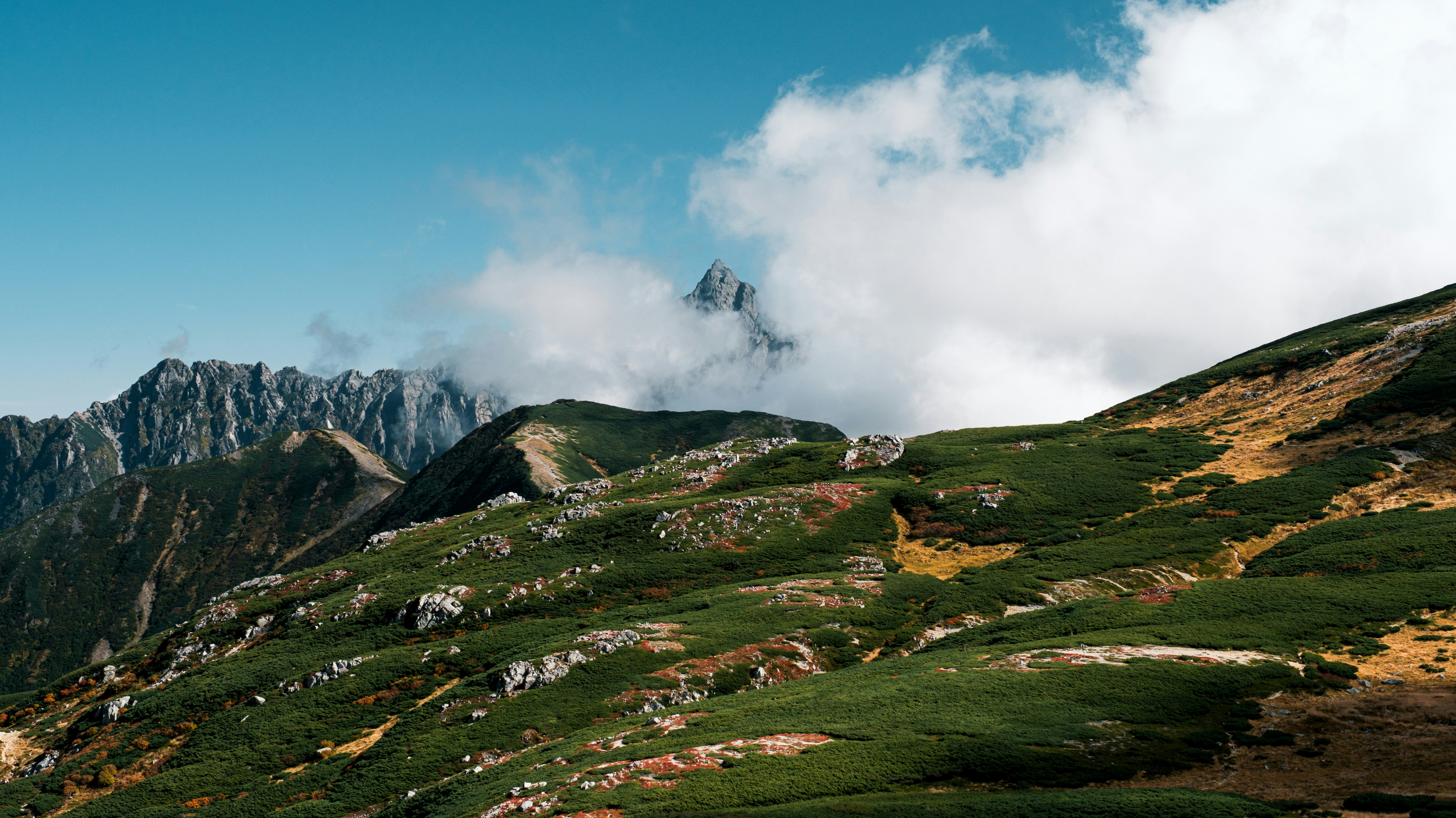 Grassy mountain slopes under a cloudy blue sky