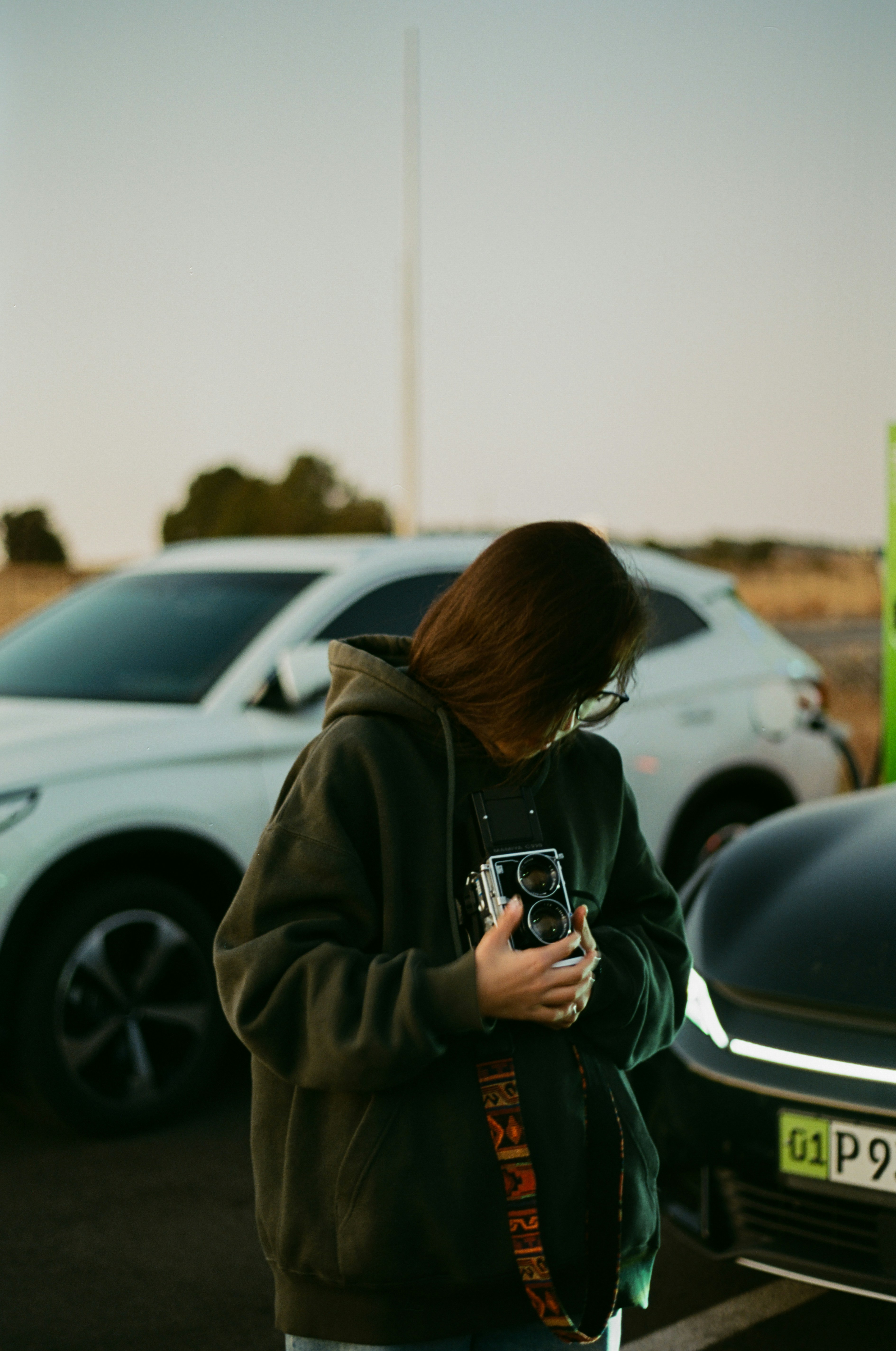 Woman holding vintage camera between two cars