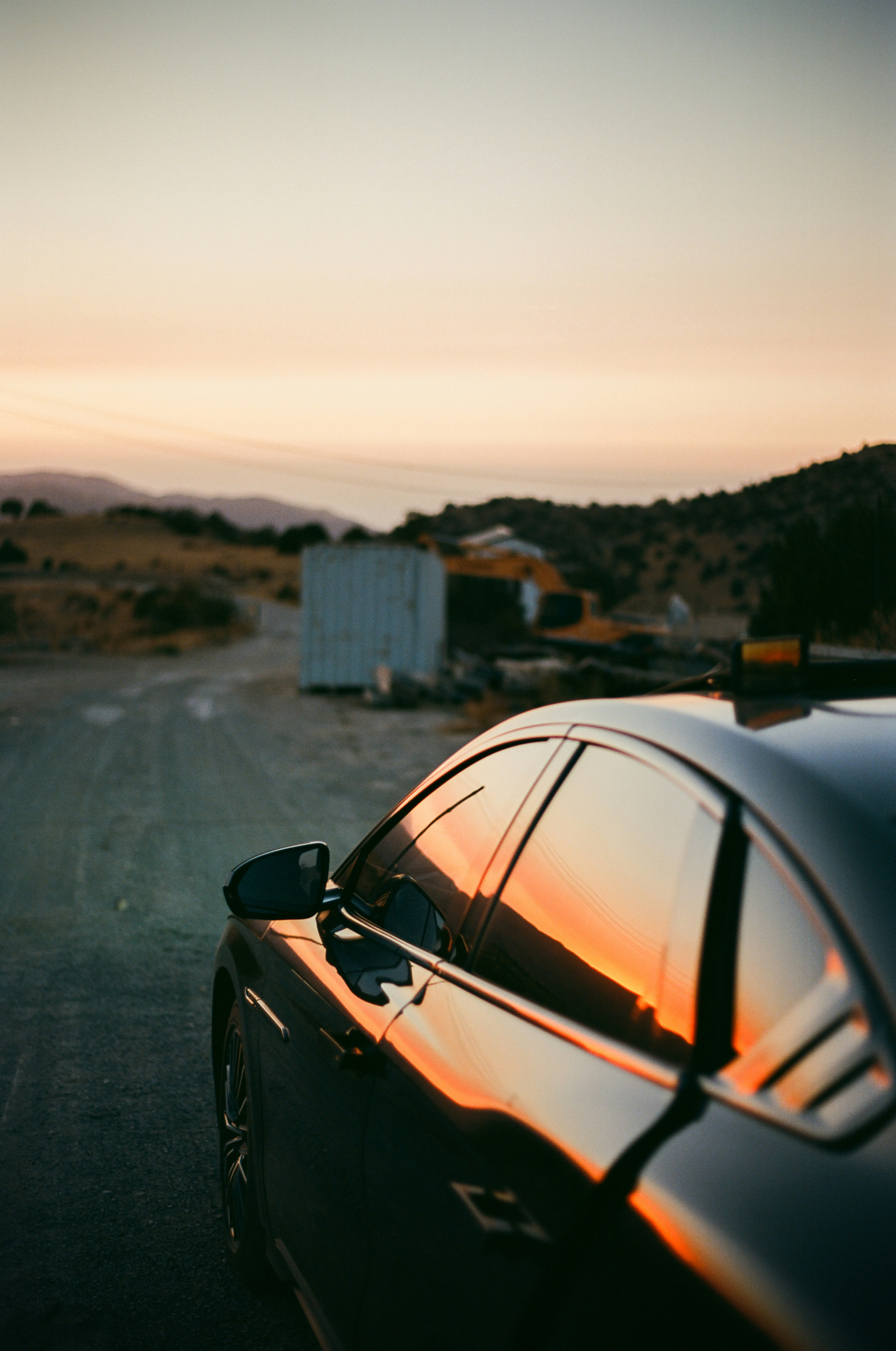 Black car reflecting sunset on a dusty road