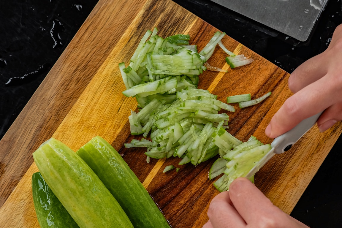 Fresh cucumbers being sliced on a wooden cutting board for refrigerator pickles