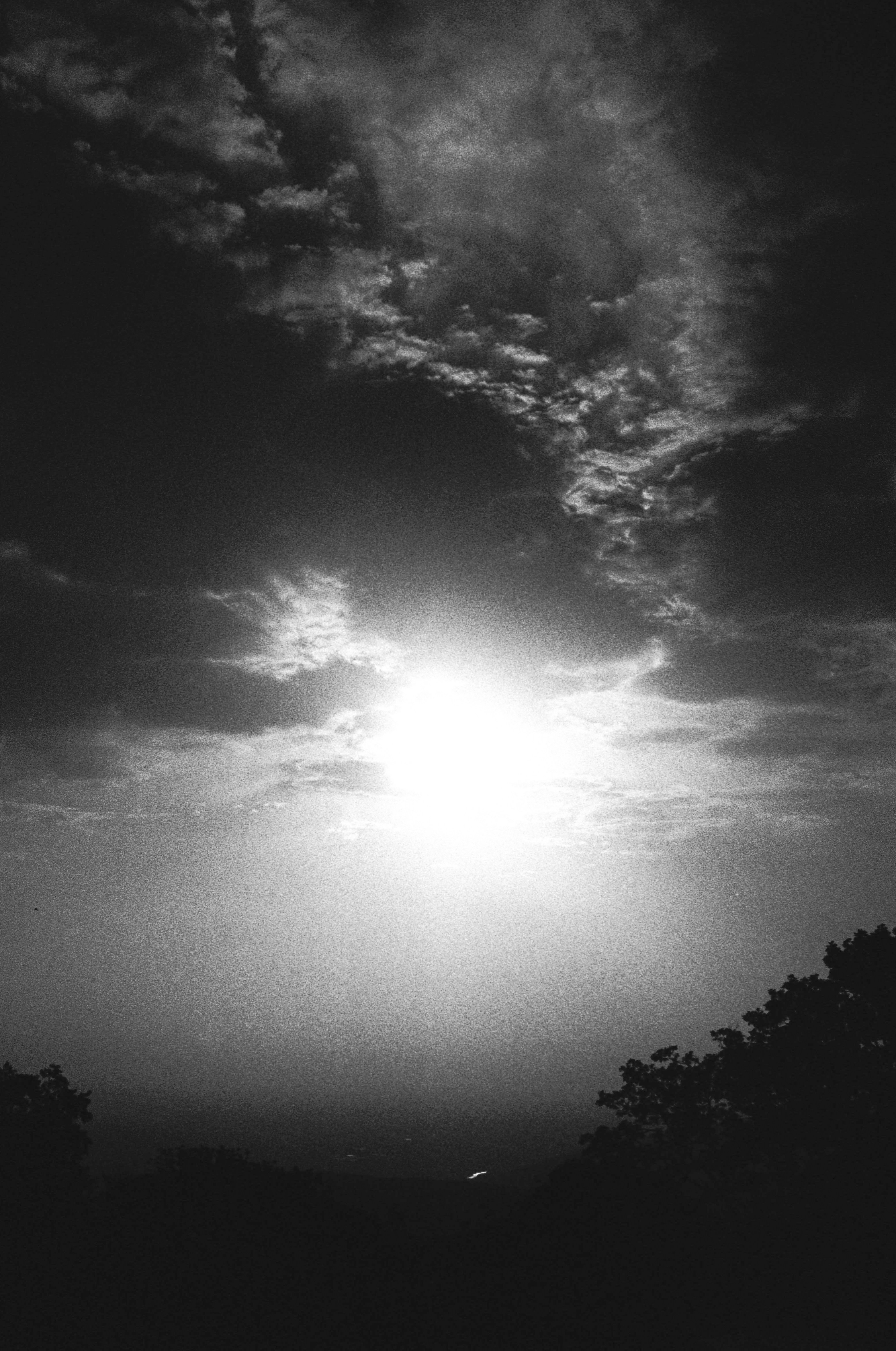 Bright sun shines through dramatic clouds at sunset.