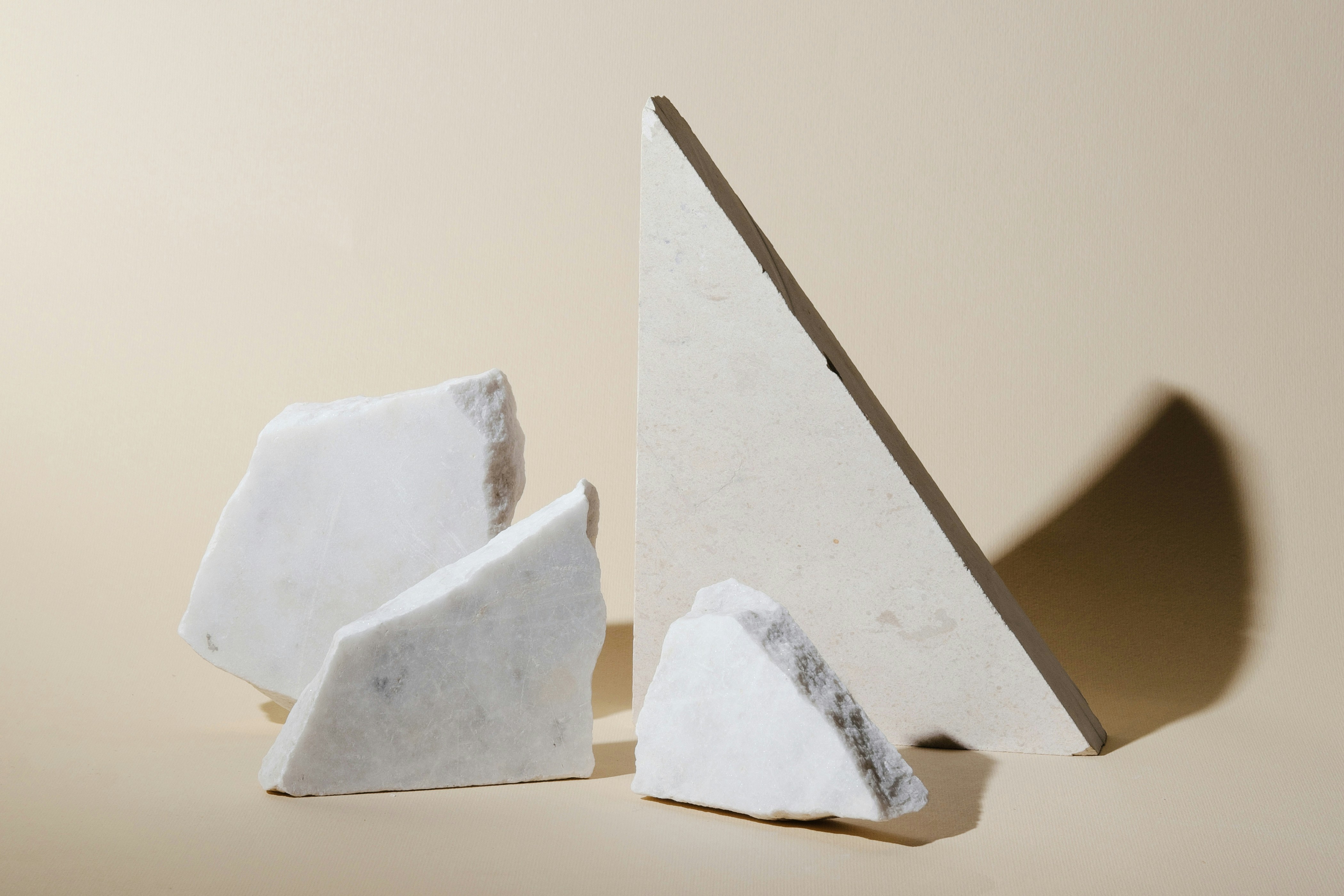 Broken white marble pieces casting shadows on beige background.