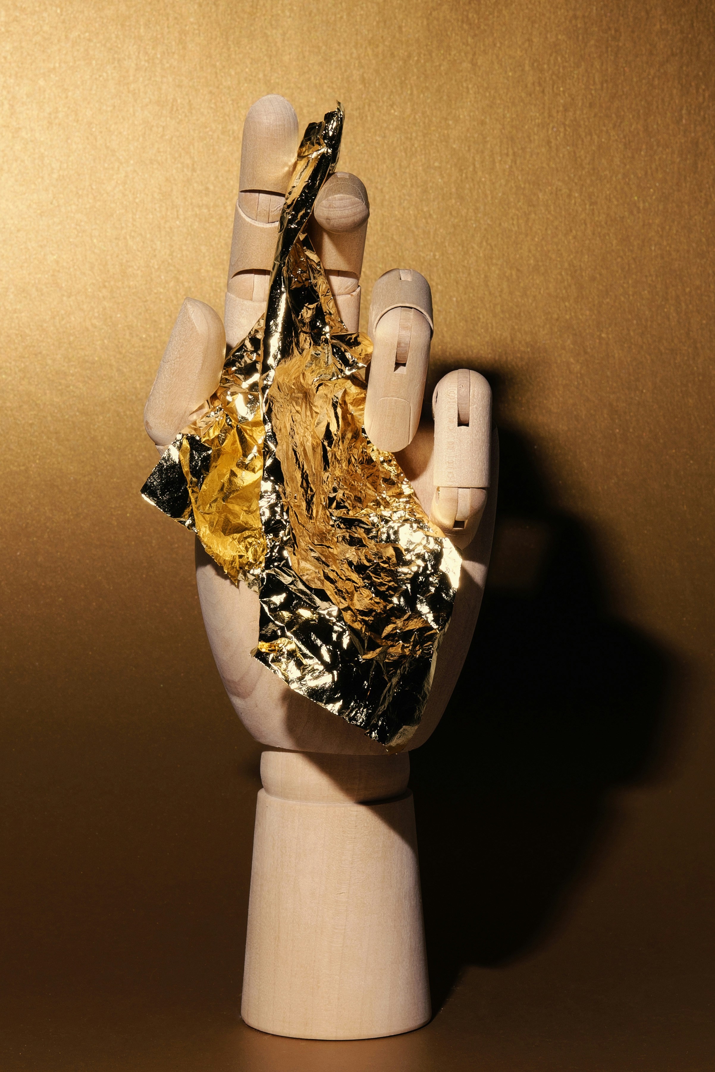 Wooden hand holding crumpled gold foil against gold background.