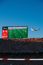 Airplane flies past stadium screen during soccer game.