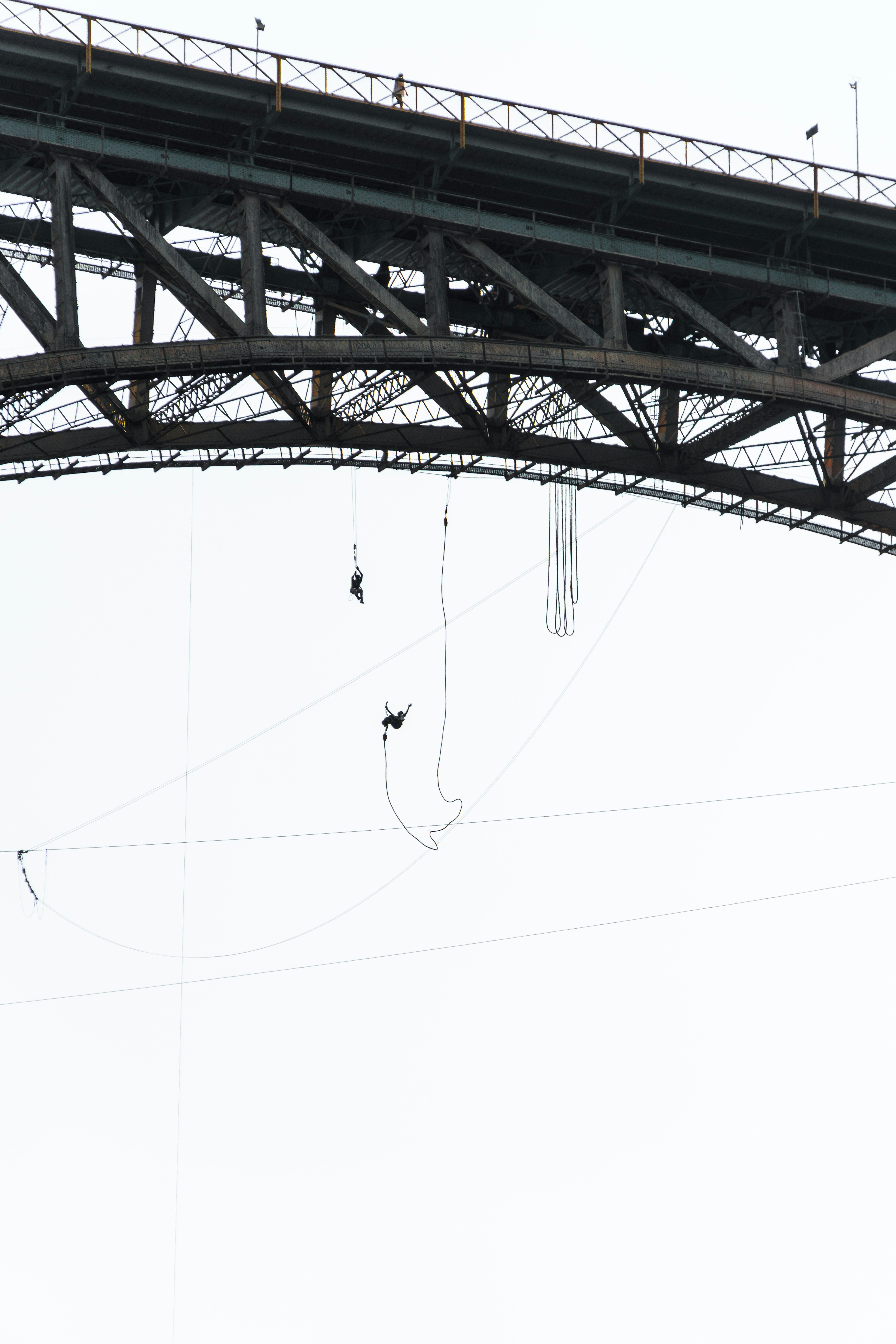 People bungee jumping from a large metal bridge.