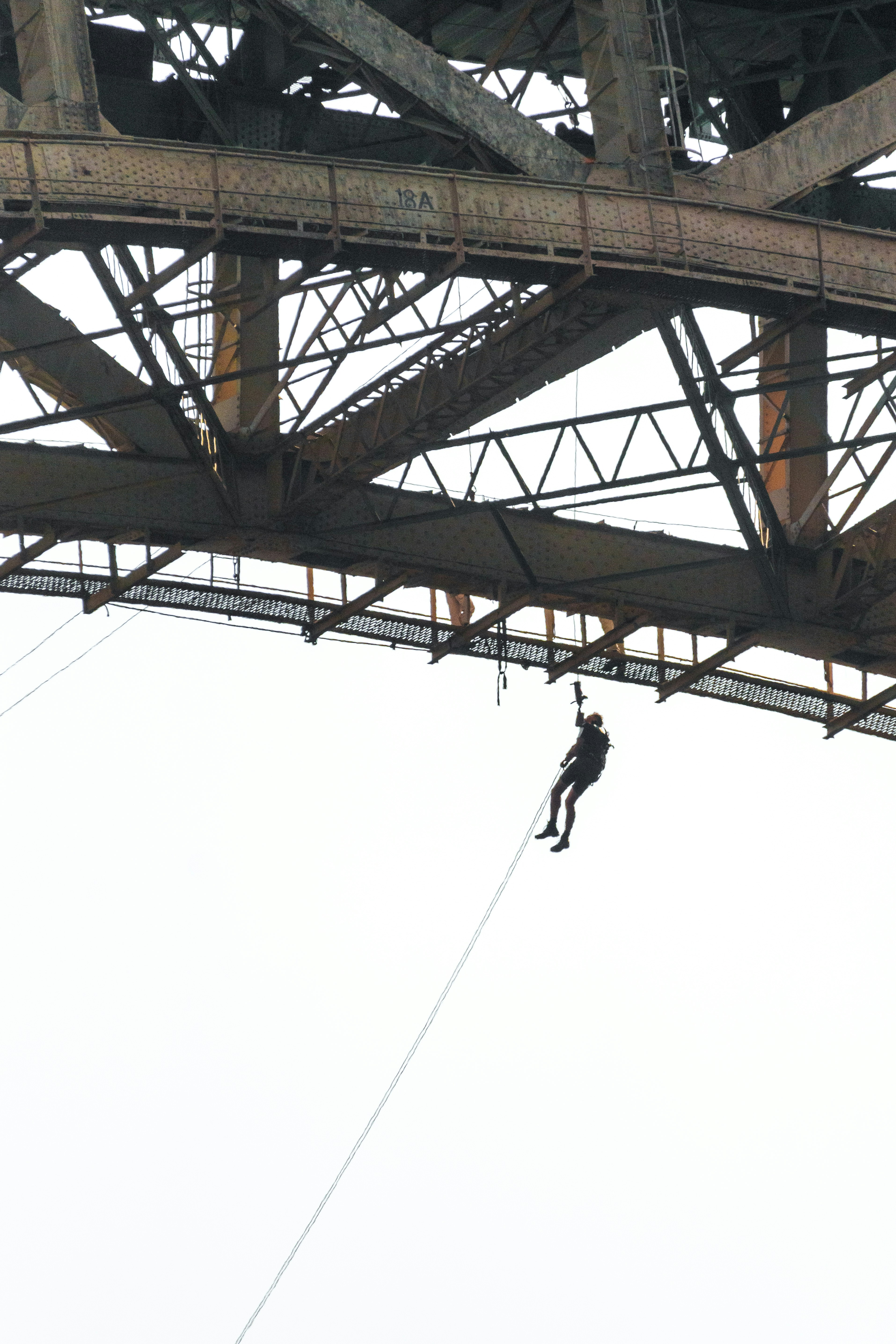 Person rappelling from a rusty metal bridge