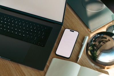 Laptop, phone, and notebook on a wooden desk.