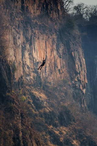Person rappelling down a steep, rocky cliff face.