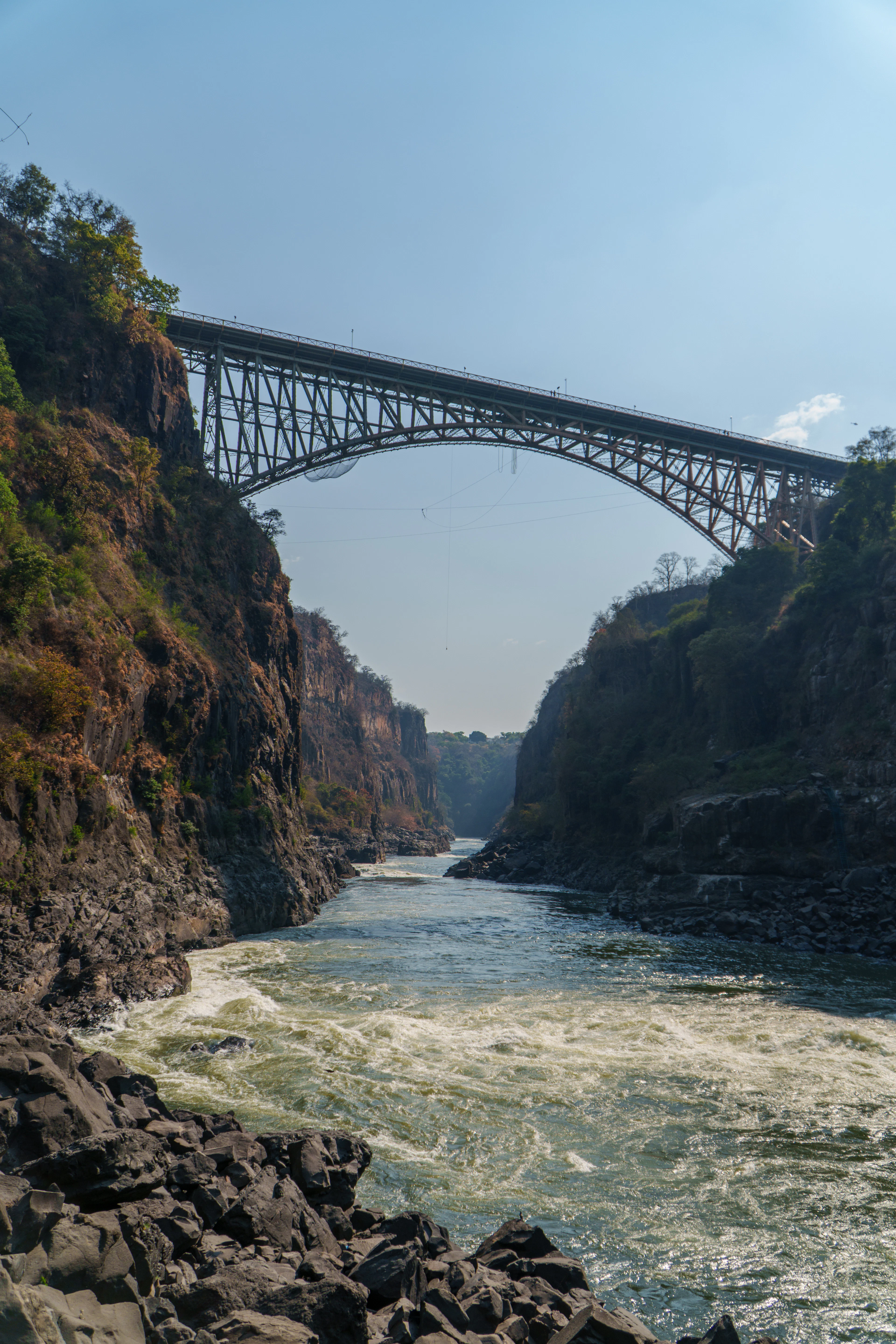 The steel arch of Victoria Falls Bridge spans the Zambezi gorge under a clear blue sky.