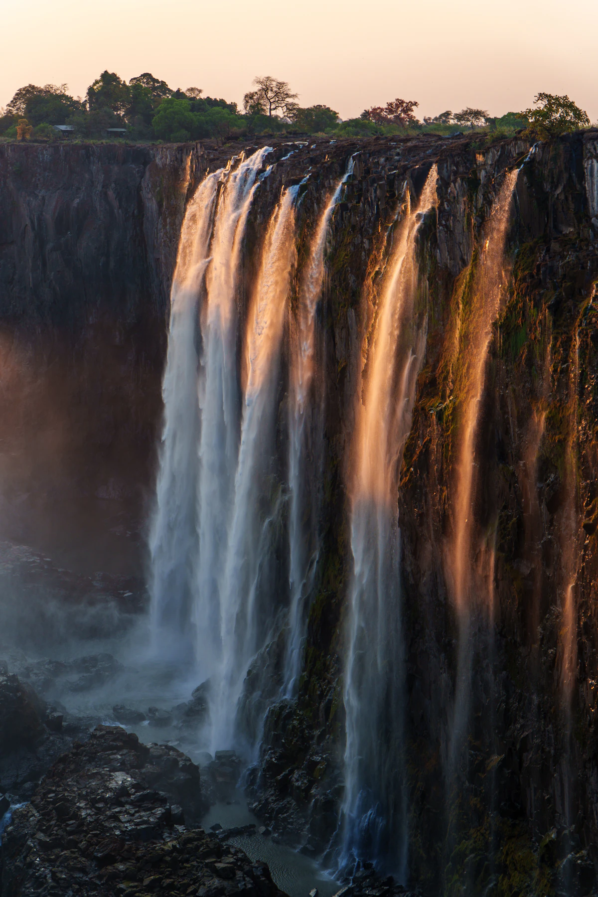 Victoria Falls glowing gold as several cascades descend over the basalt cliff