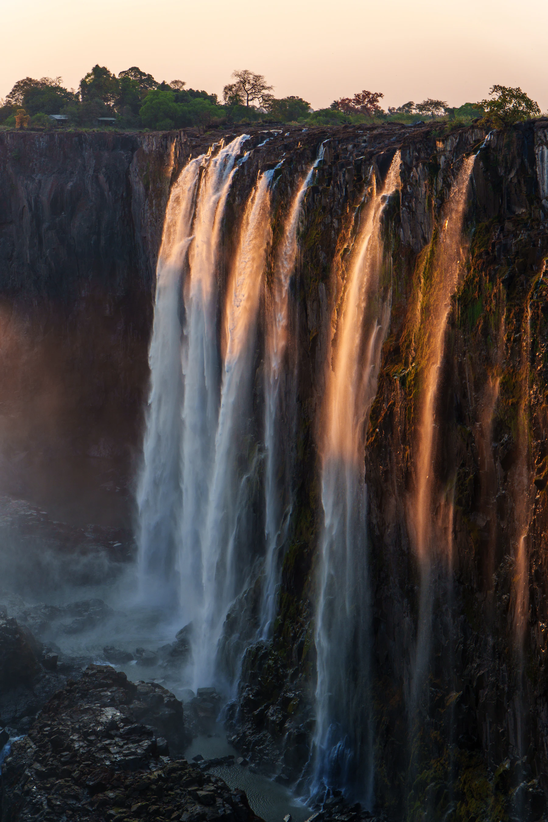 Victoria Falls glowing gold as several cascades descend over the basalt cliff