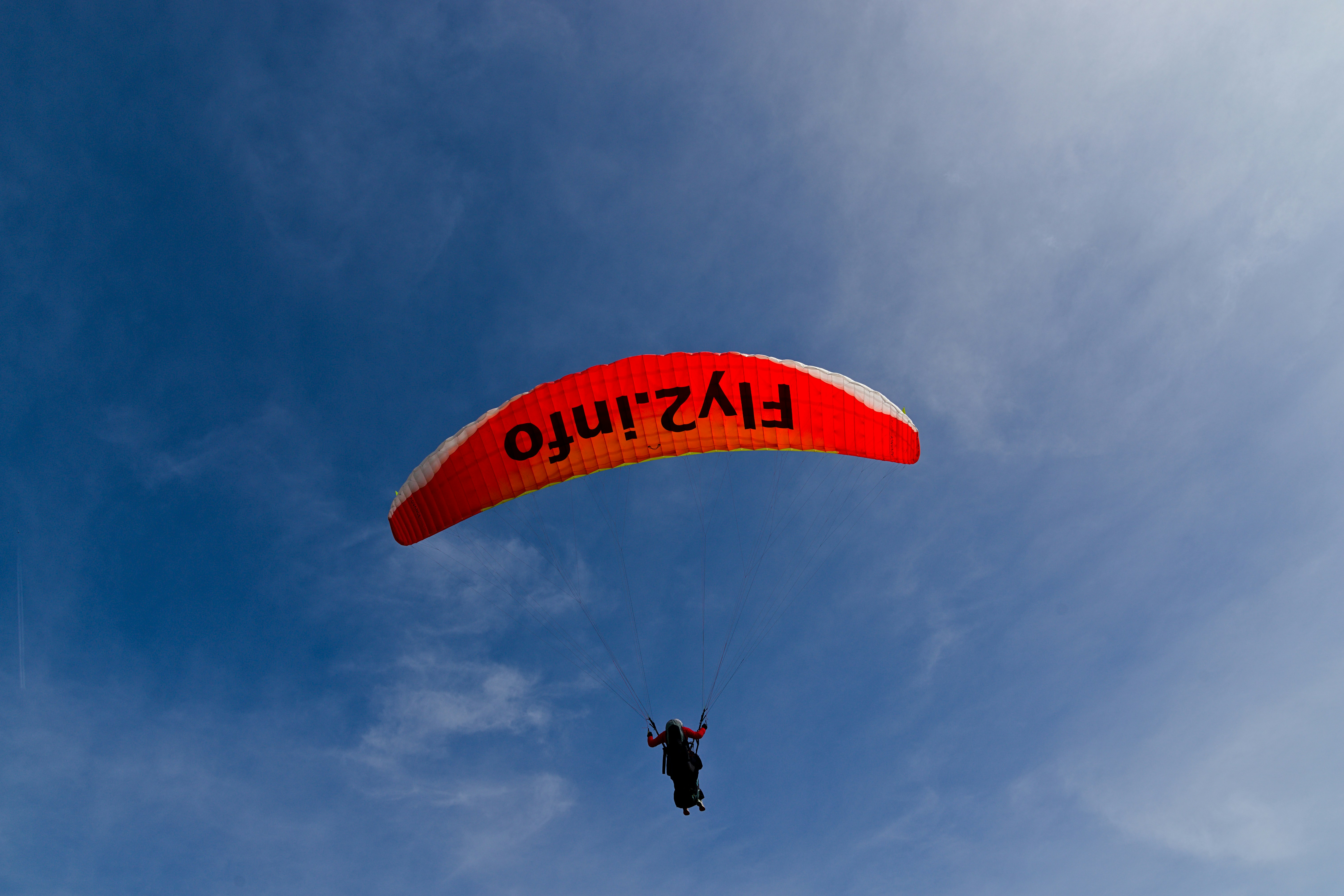 Paraglider with orange and white wing against blue sky