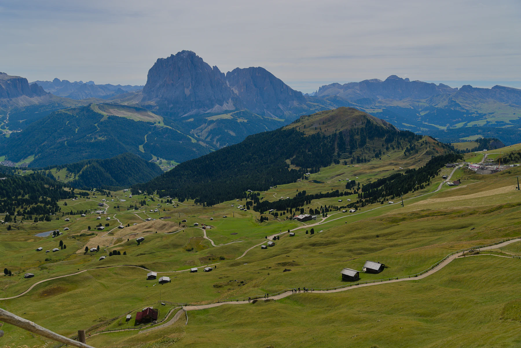 Alpenweide met verspreide hutjes en paden, rotsmassief aan de horizon