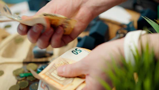 Hands counting euro banknotes with coins scattered around.