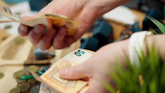 Hands counting euro banknotes with coins scattered around.