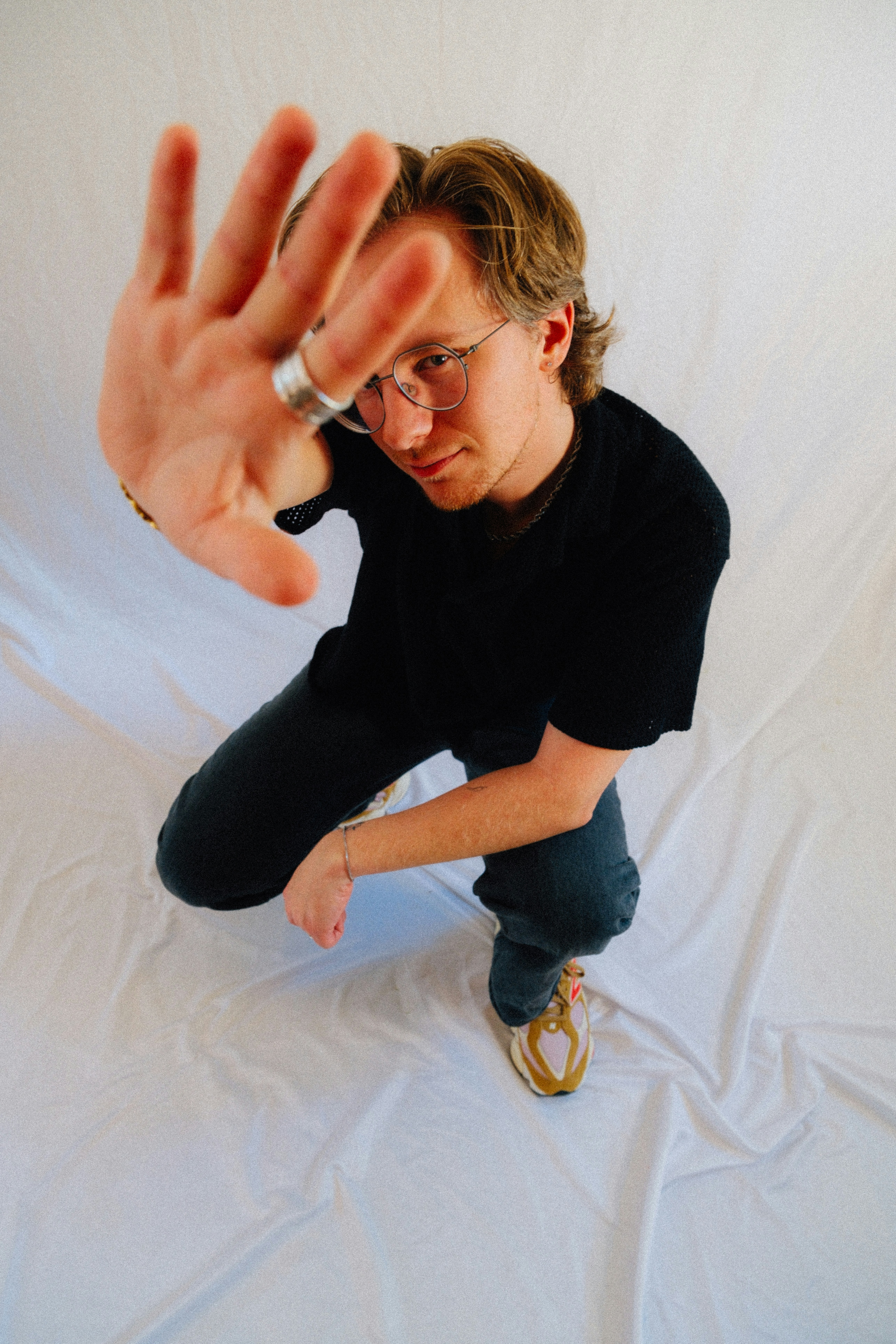 Mann im schwarzen Hemd hält die Hand hoch und schaut in die Kamera.