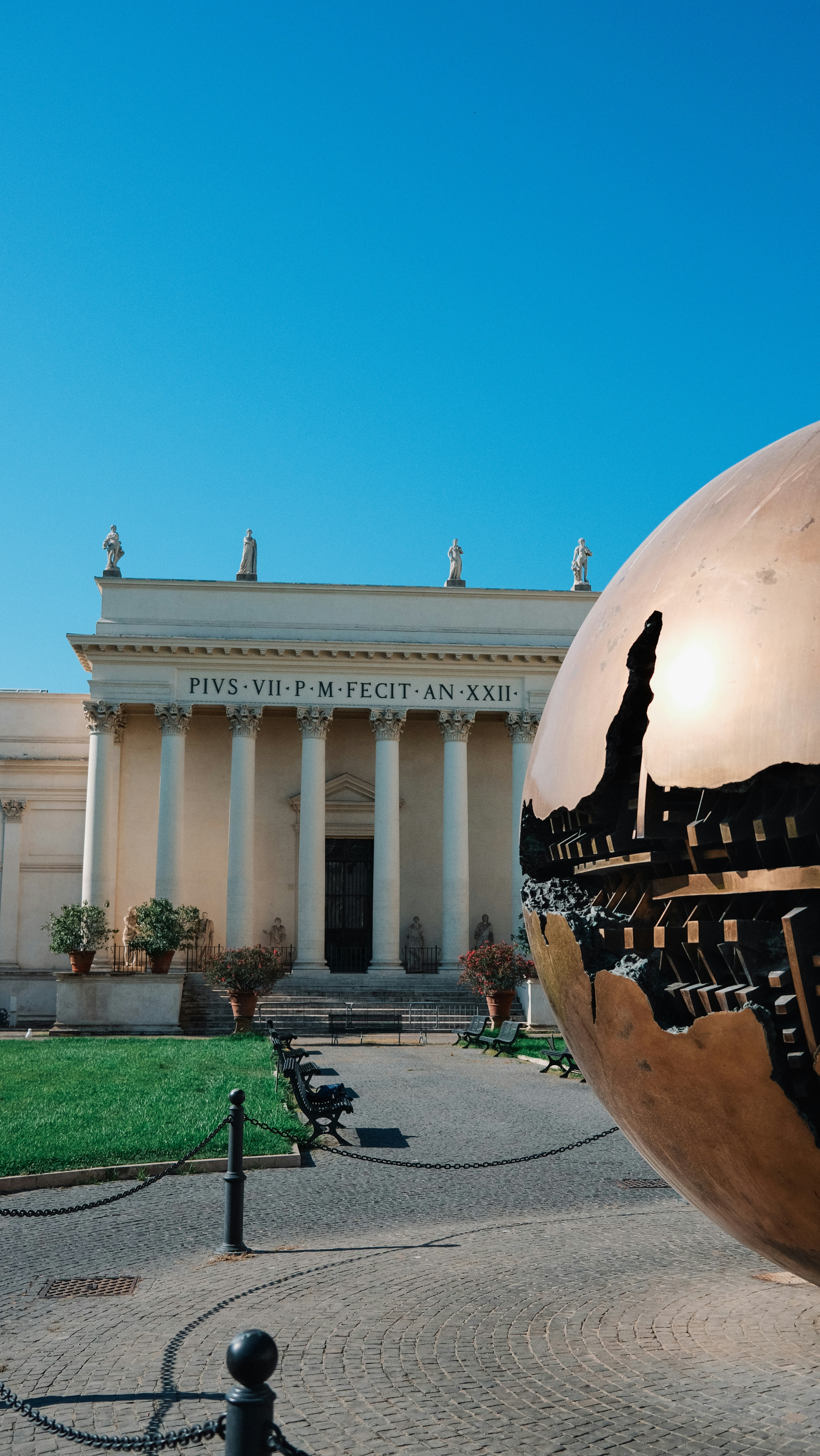 A large bronze sphere in front of a classical building.