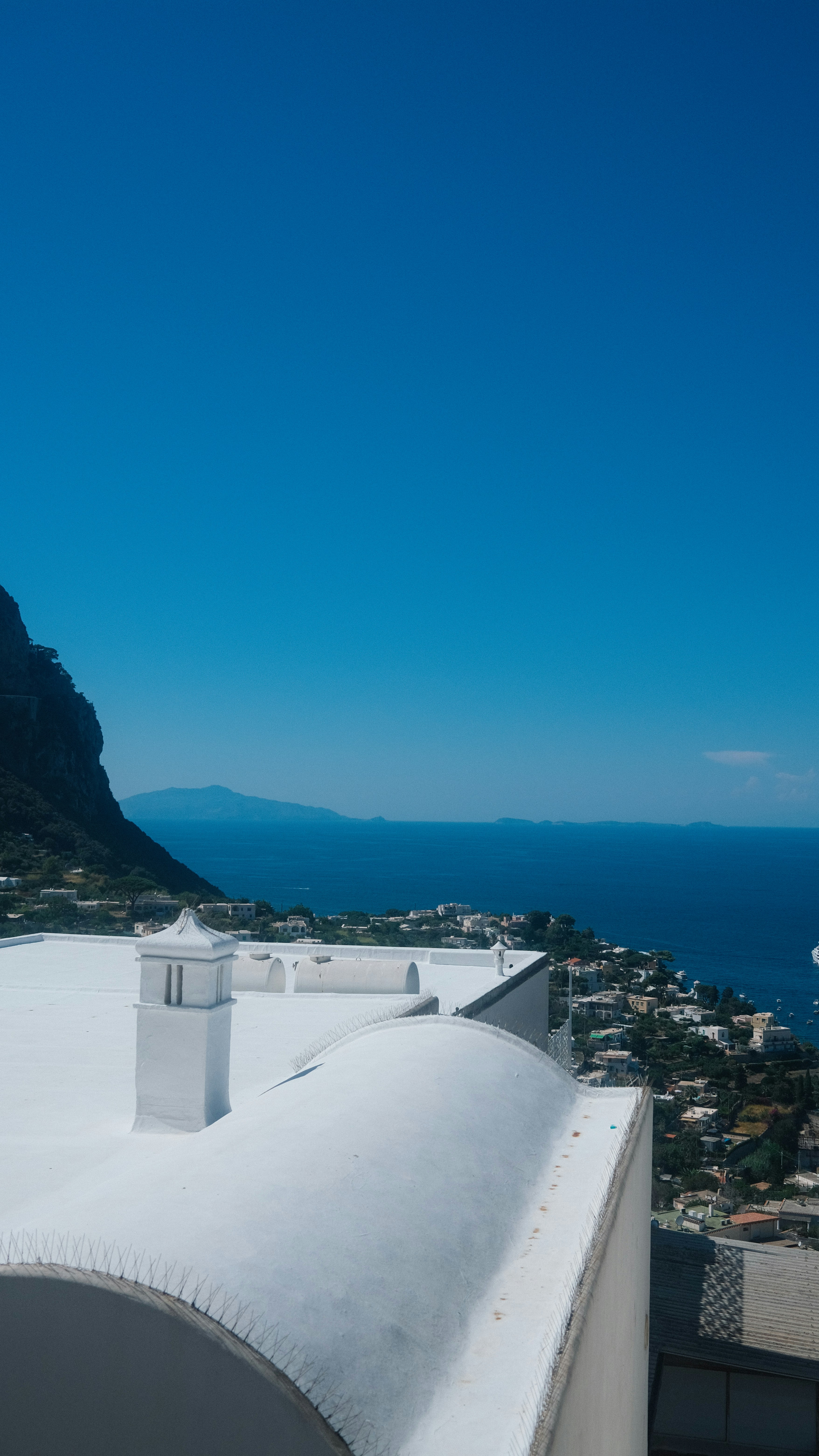 White rooftops overlook a coastal town and blue ocean.