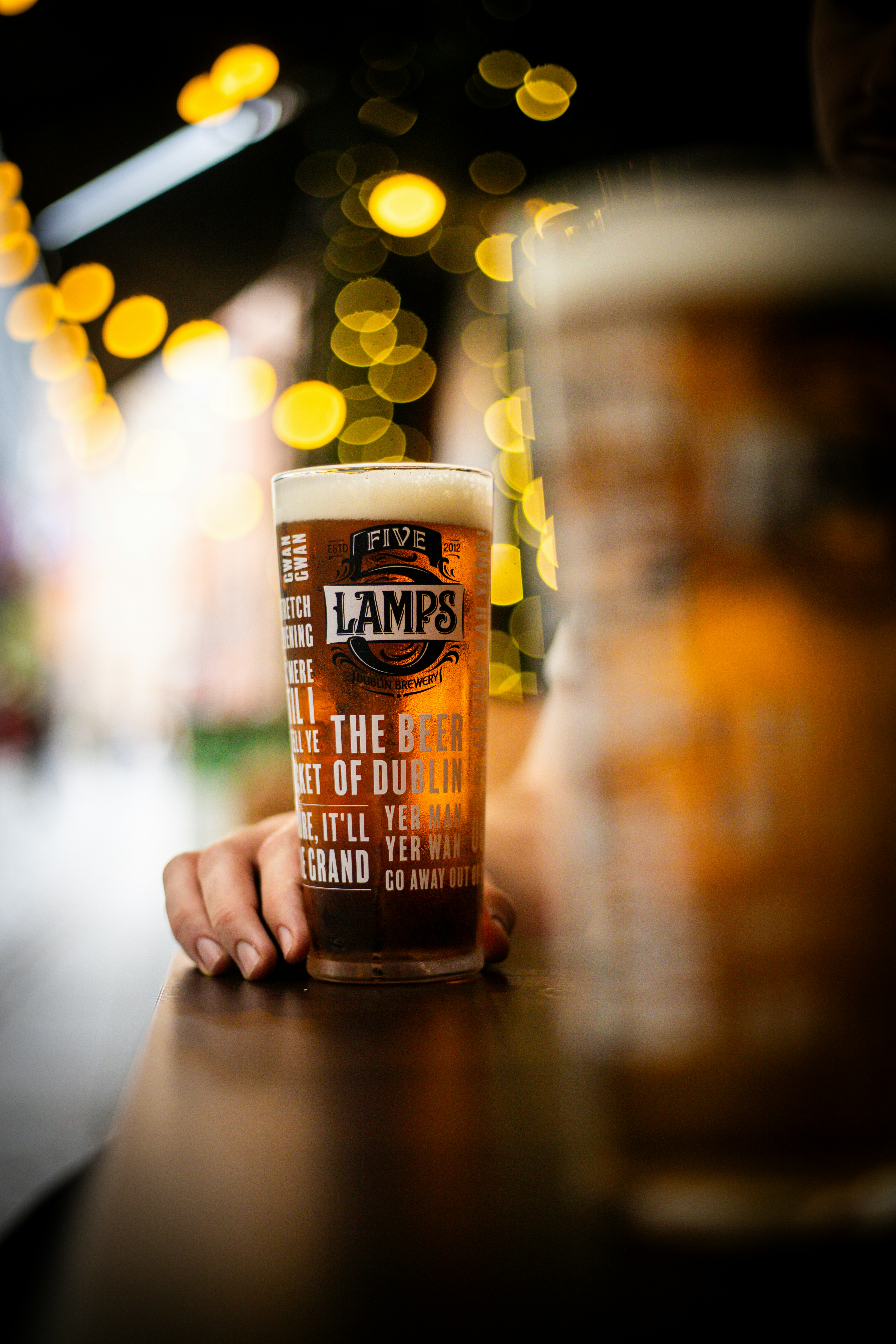 Hand holding a pint of beer with bokeh lights