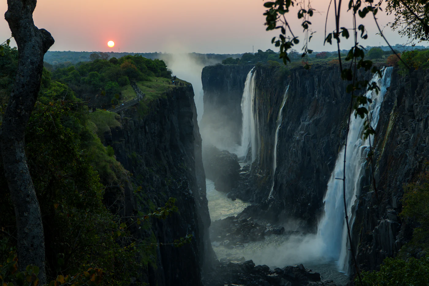 Victoria Falls at sunrise framed by lush green foliage
