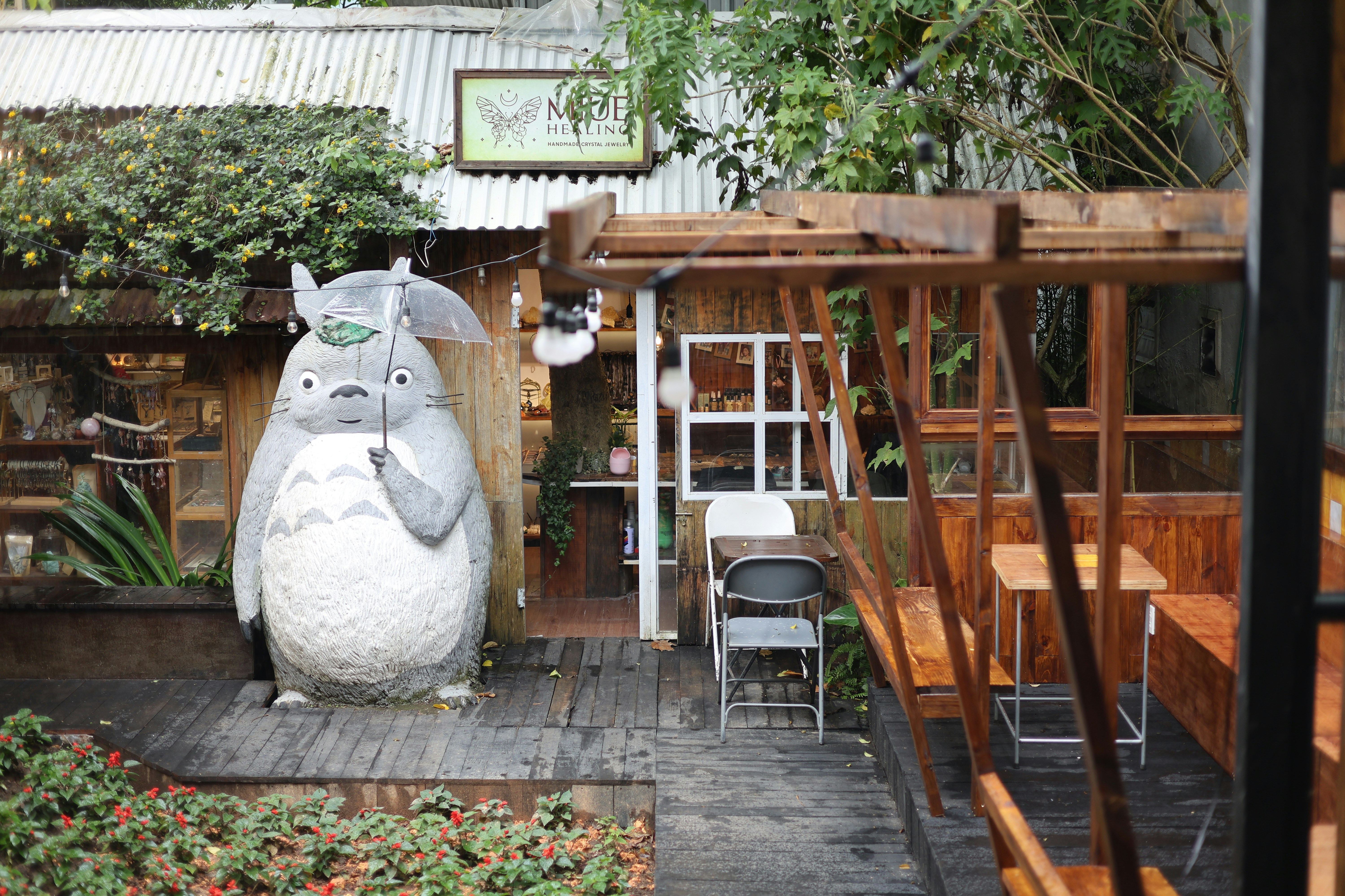 Totoro statue holding an umbrella on a wooden deck.