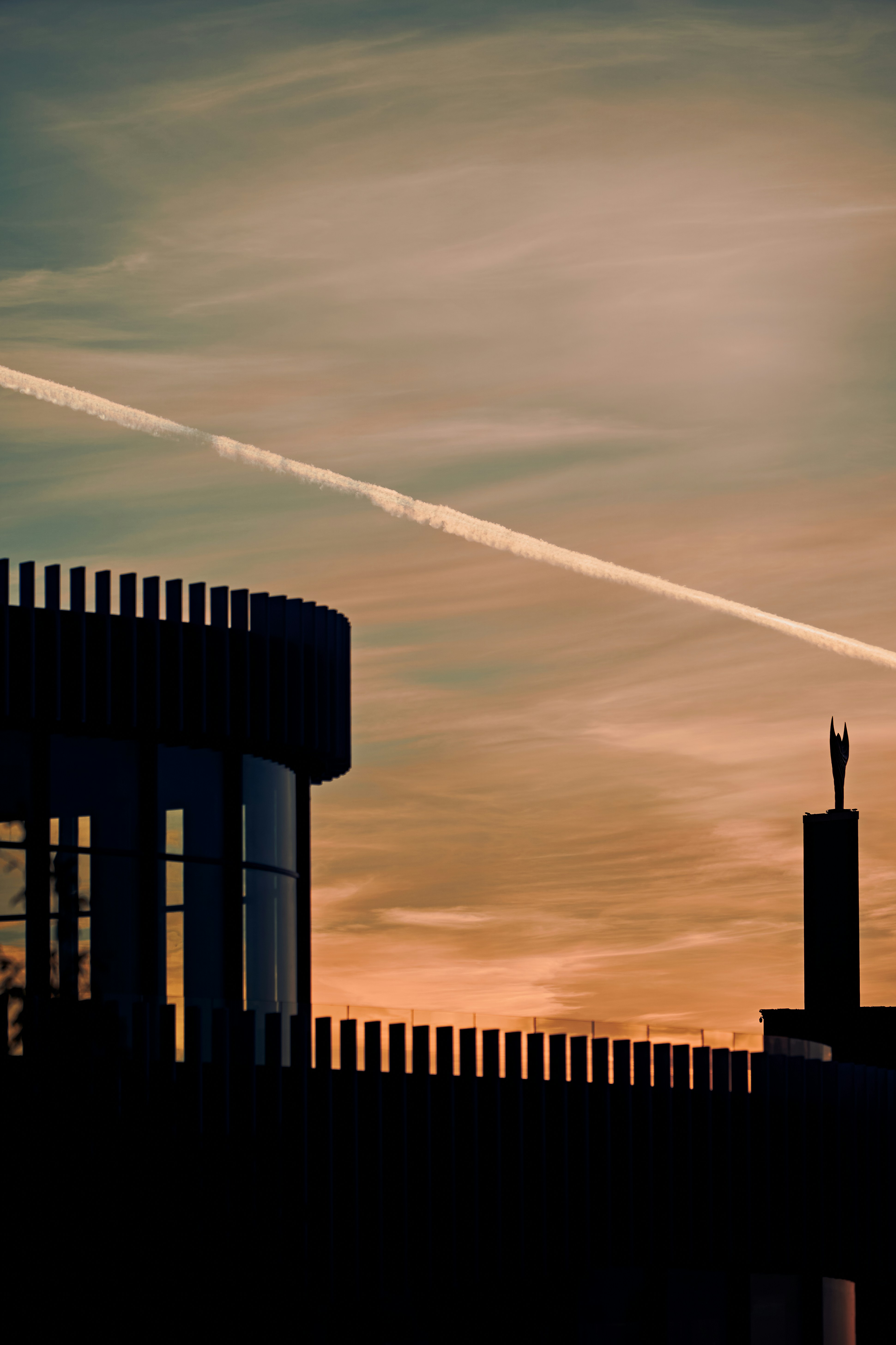 Silhouette of building against sunset sky with contrail