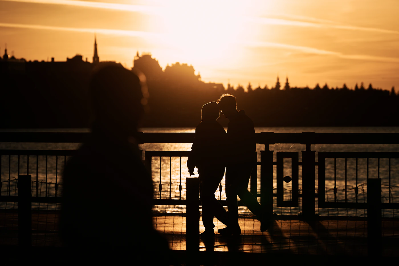 Romantic couple silhouetted together against a warm golden sunset reflecting over a calm body of water