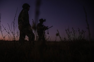Two soldiers walk through a field at dusk.