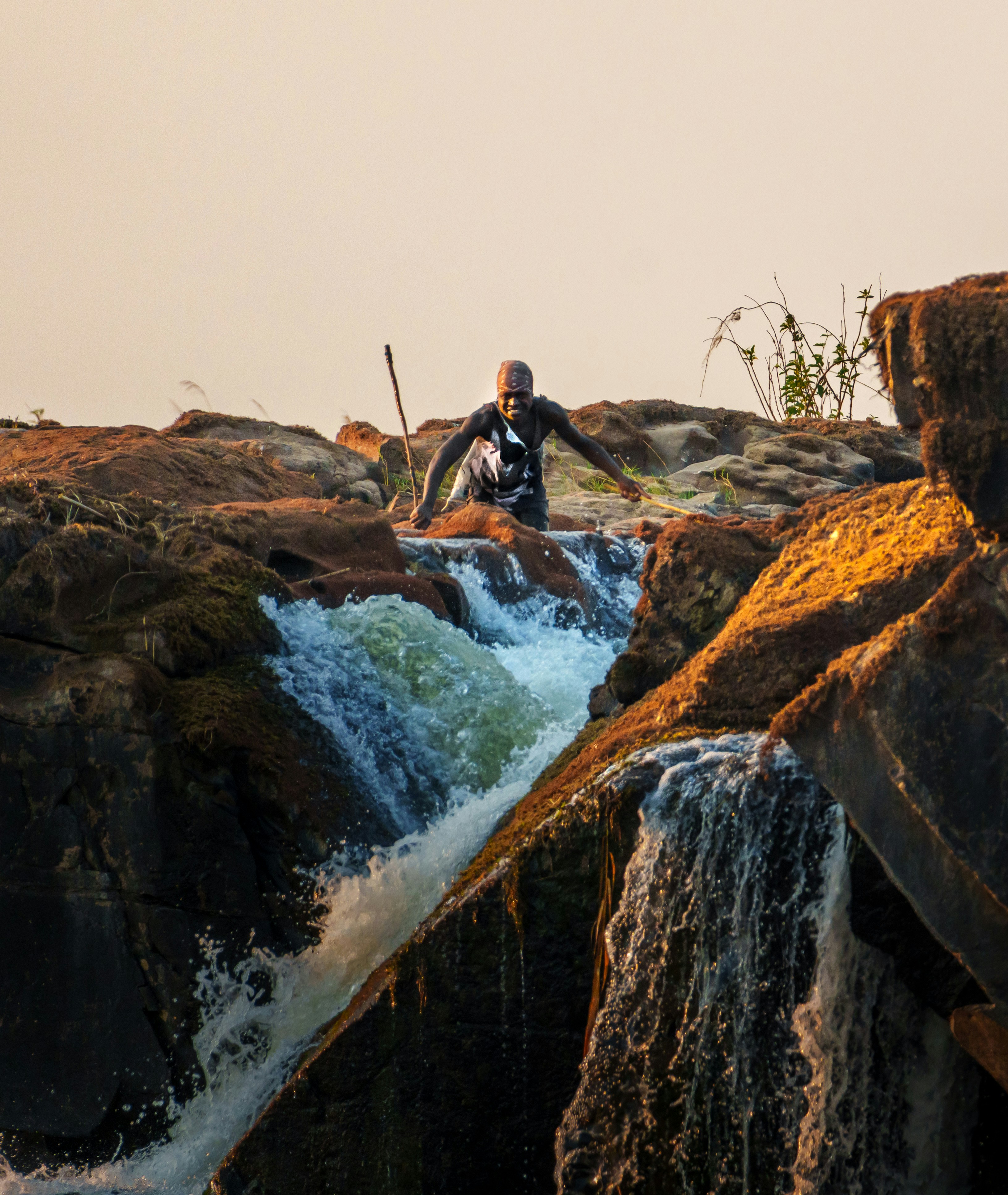 Hombre con palo sube cascada rocosa en cascada