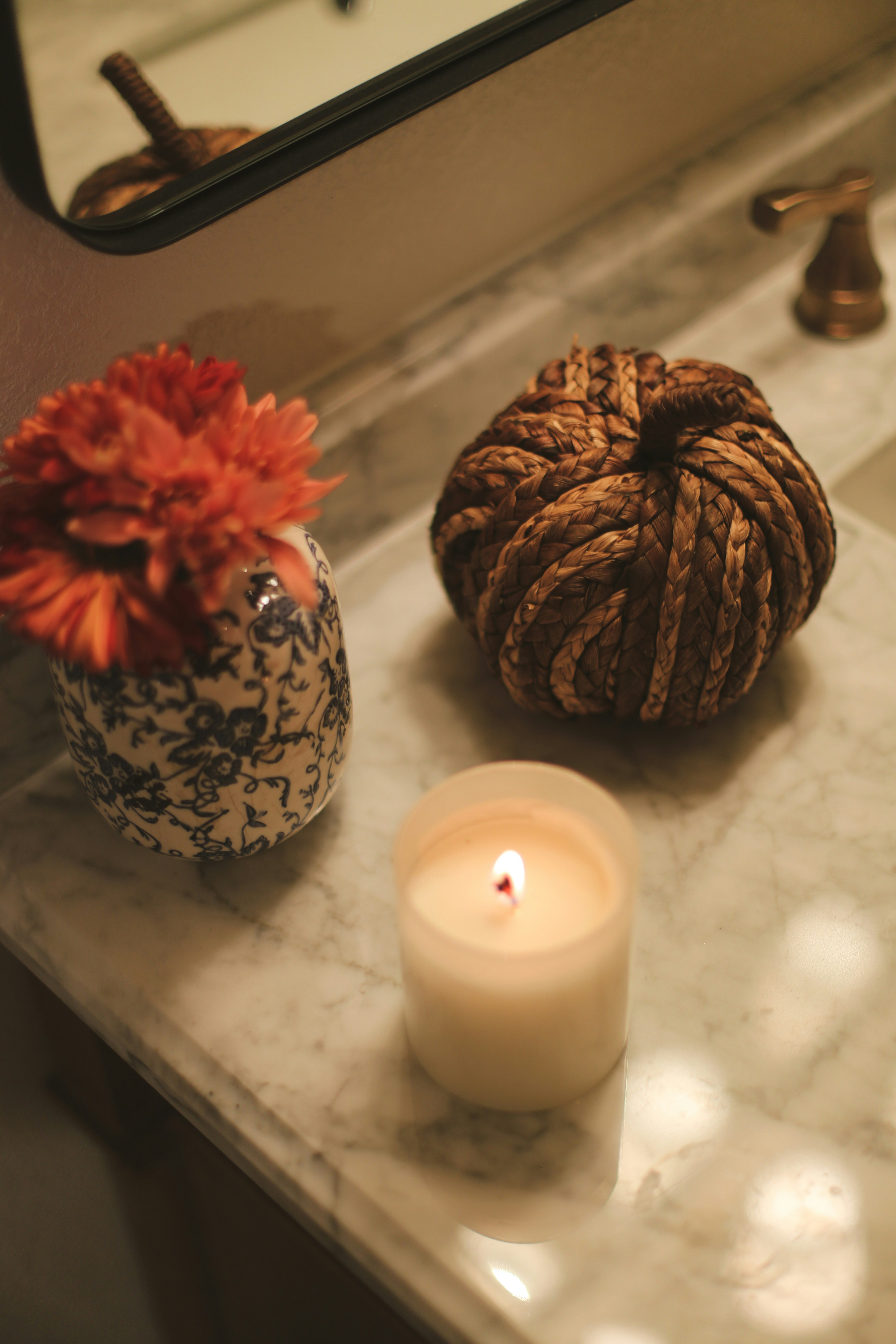 Lit candle, decorative knot, and flower in vase on counter.