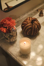 Lit candle, decorative knot, and flower in vase on counter.