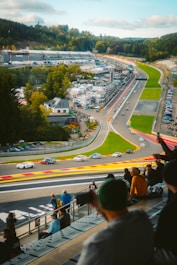 Race cars speed along a winding track with spectators watching.