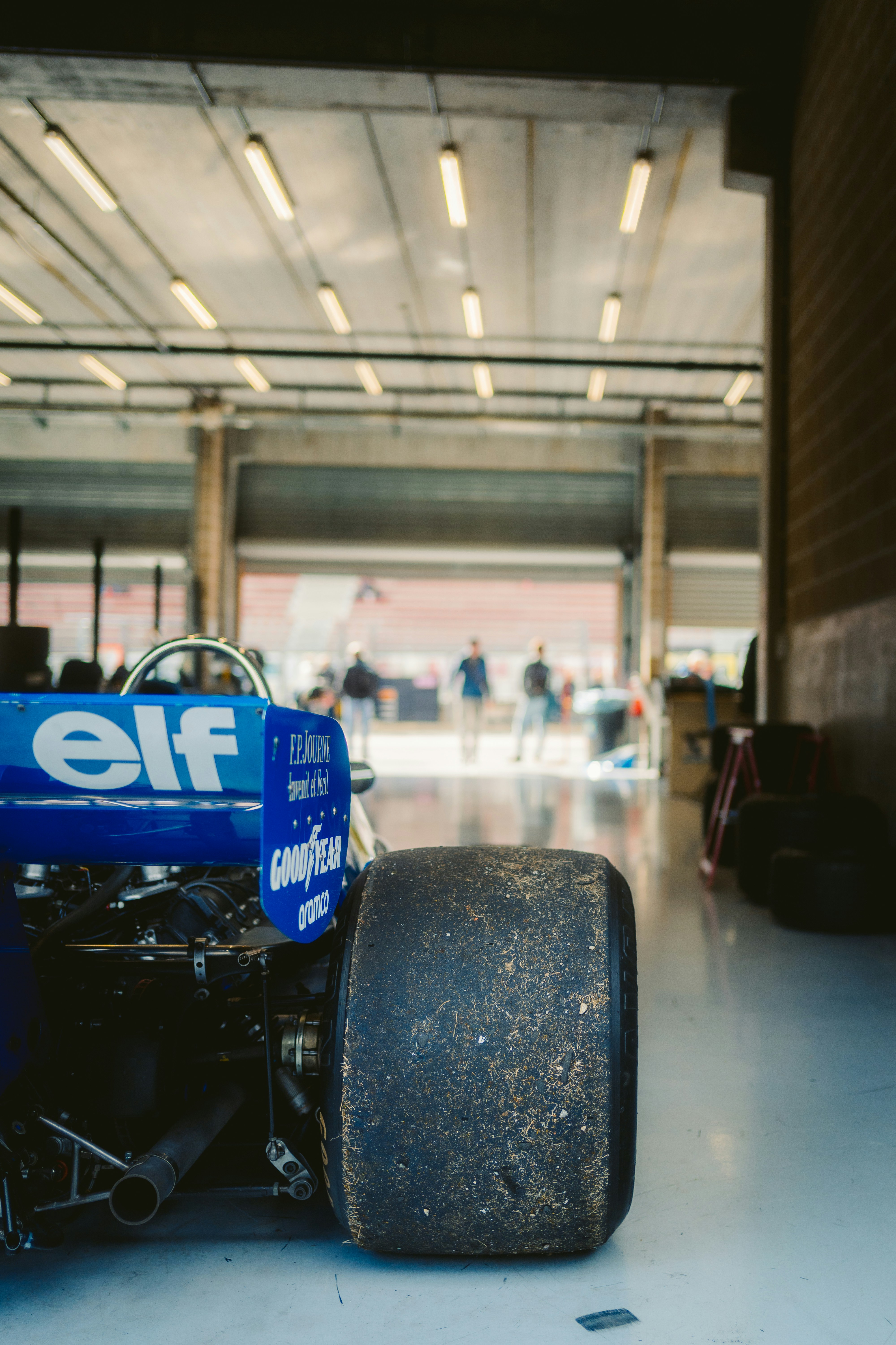 Race car in garage with open doors and people.