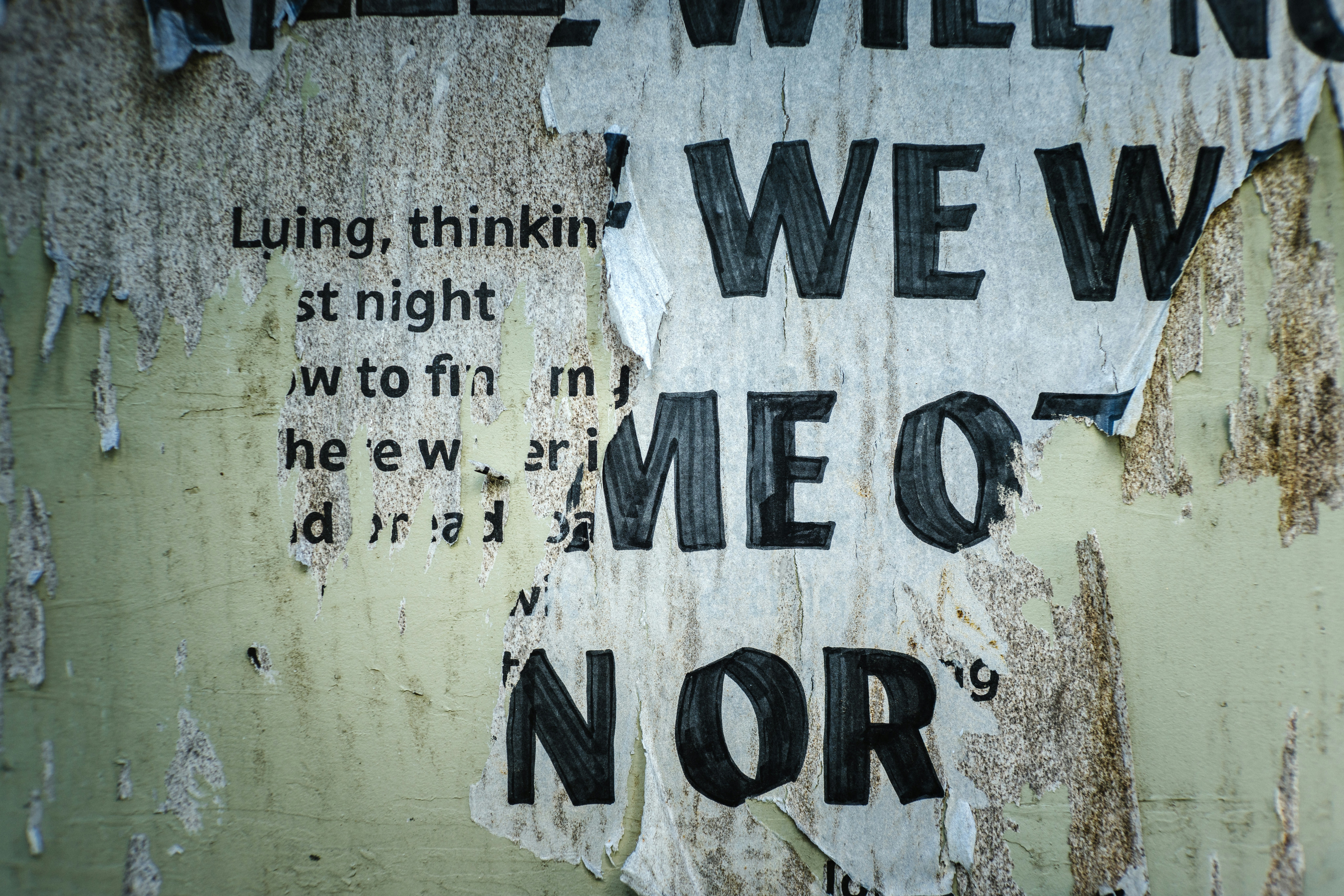 Torn posters with black text on weathered wall.