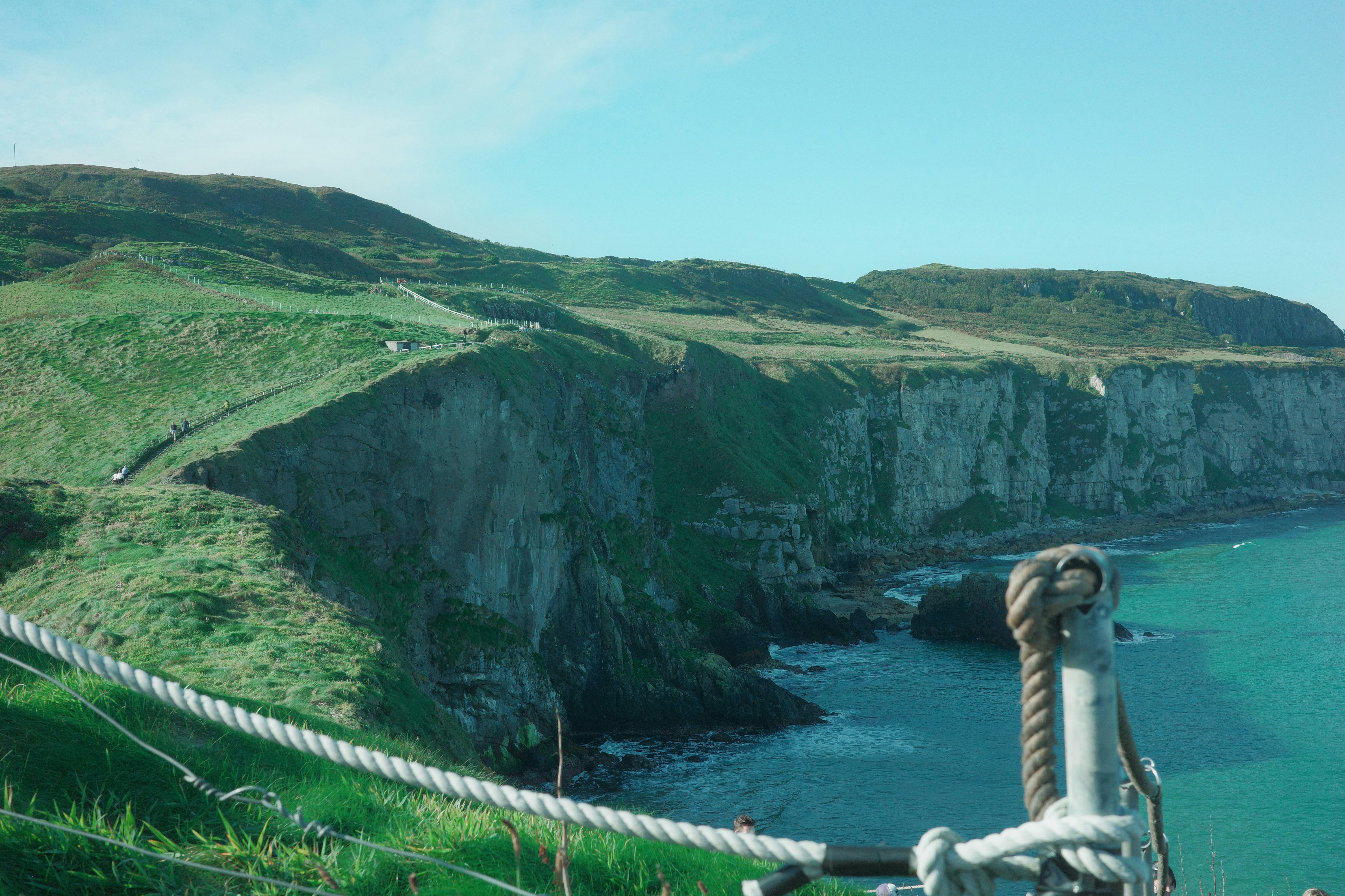 Green cliffs overlooking the ocean with a rope bridge.