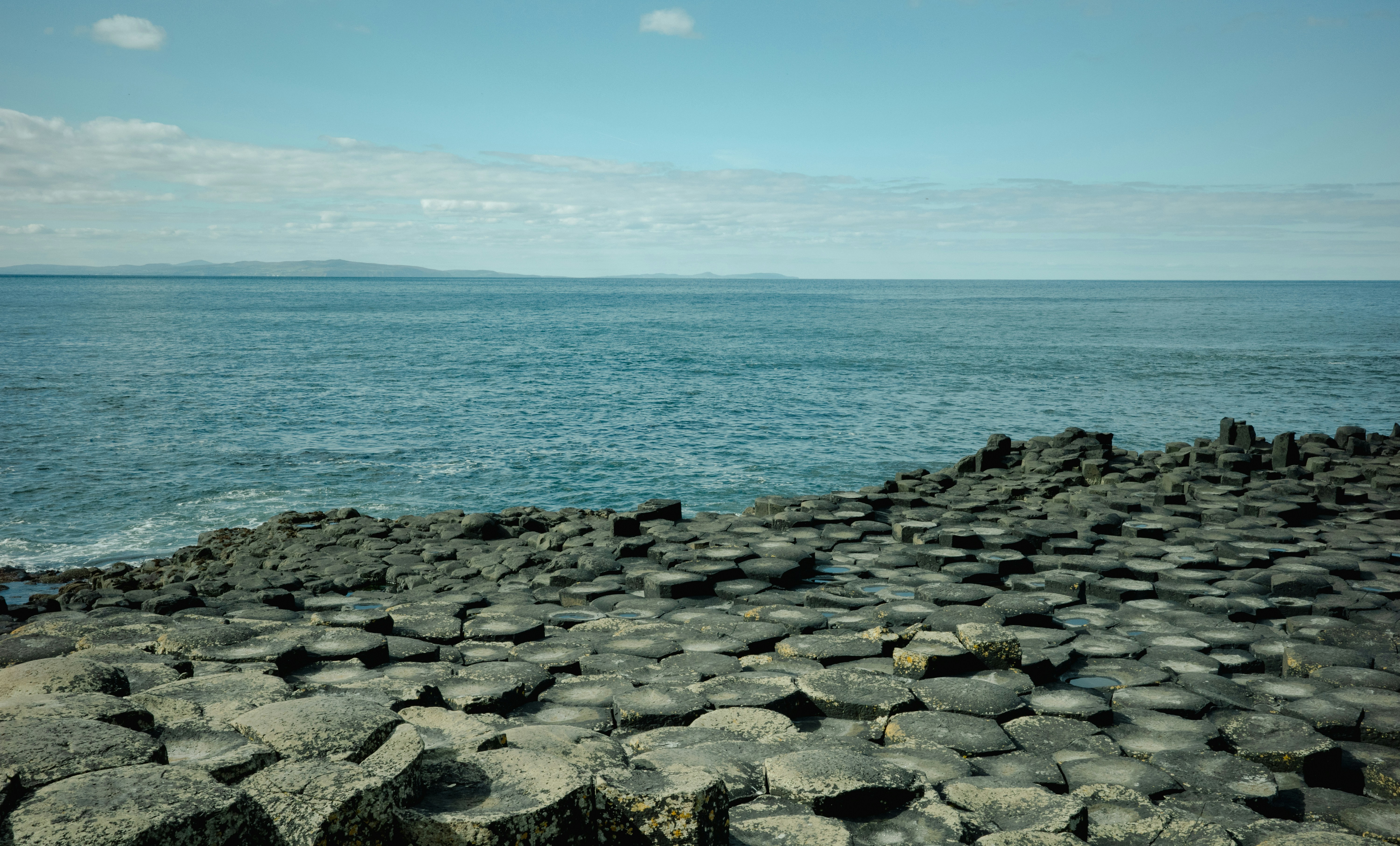 Hexagonal basalt columns at the Giant's Causeway stretching into the Atlantic Ocean under a blue sky — Northern Ireland's only UNESCO World Heritage Site