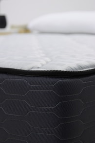 Close-up of a dark gray mattress with white bedding.