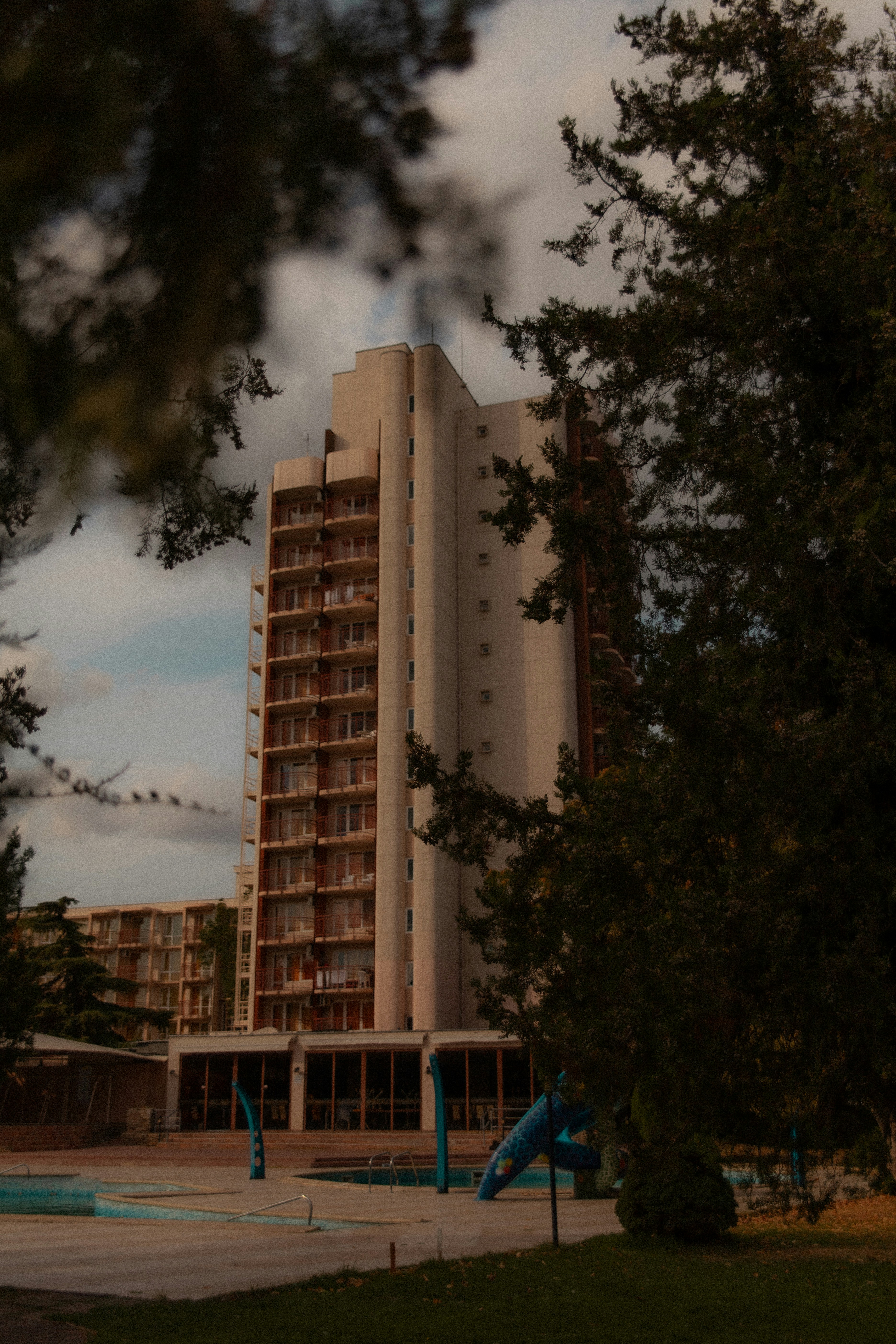 Tall concrete building with balconies and trees.