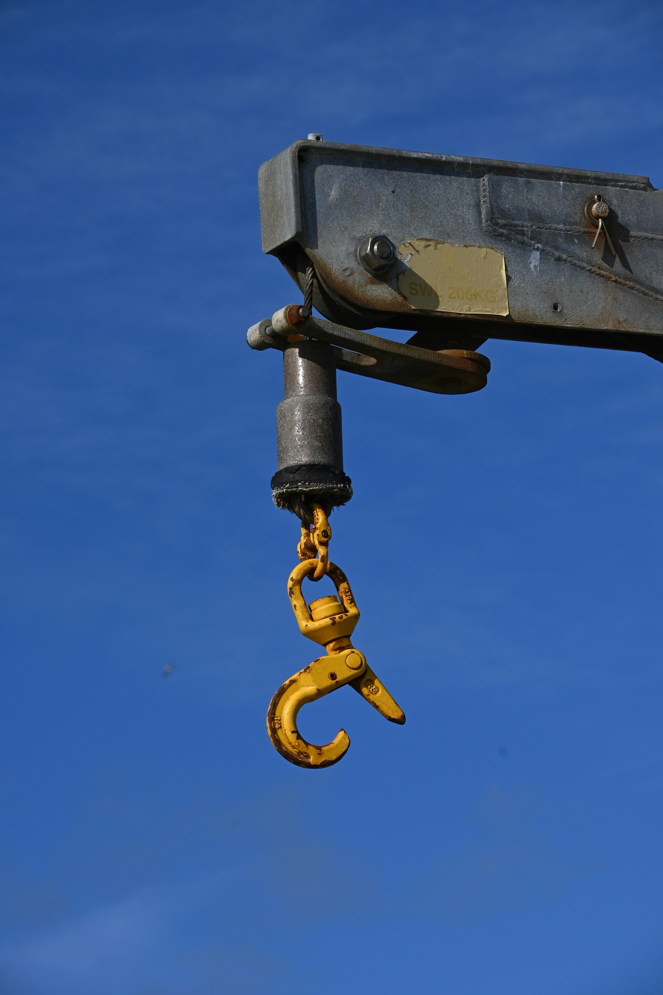 A yellow hook hangs from a crane arm