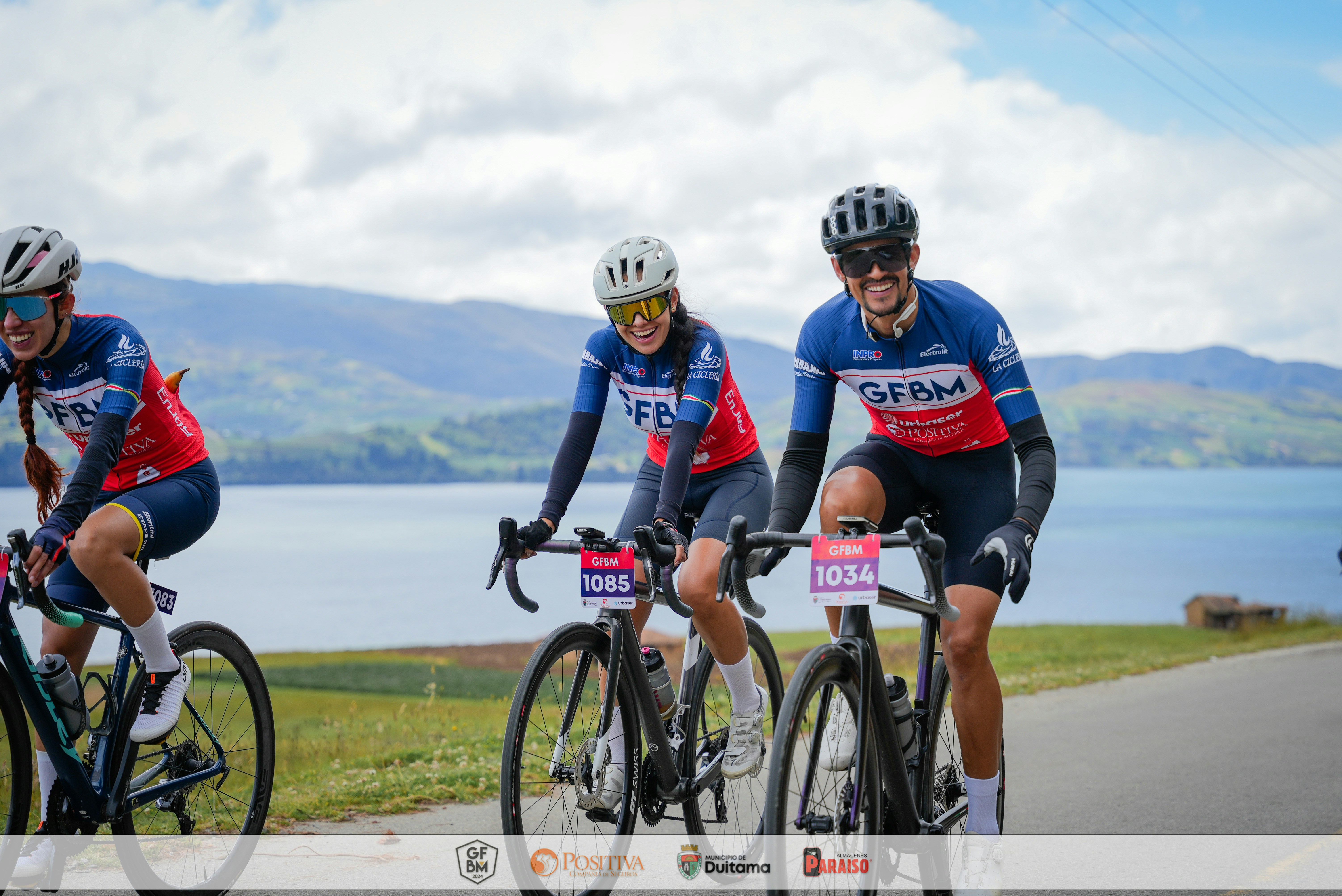 Three cyclists race along a scenic lakeside road.