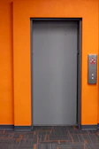 A closed gray door on an orange wall.