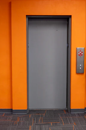 A closed gray door on an orange wall.